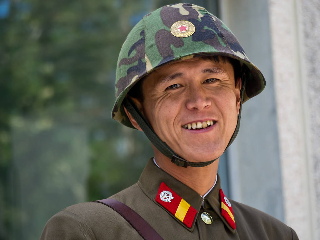 一名開朗的士兵，戴著迷彩頭盔和帶有紅色徽章的軍服。