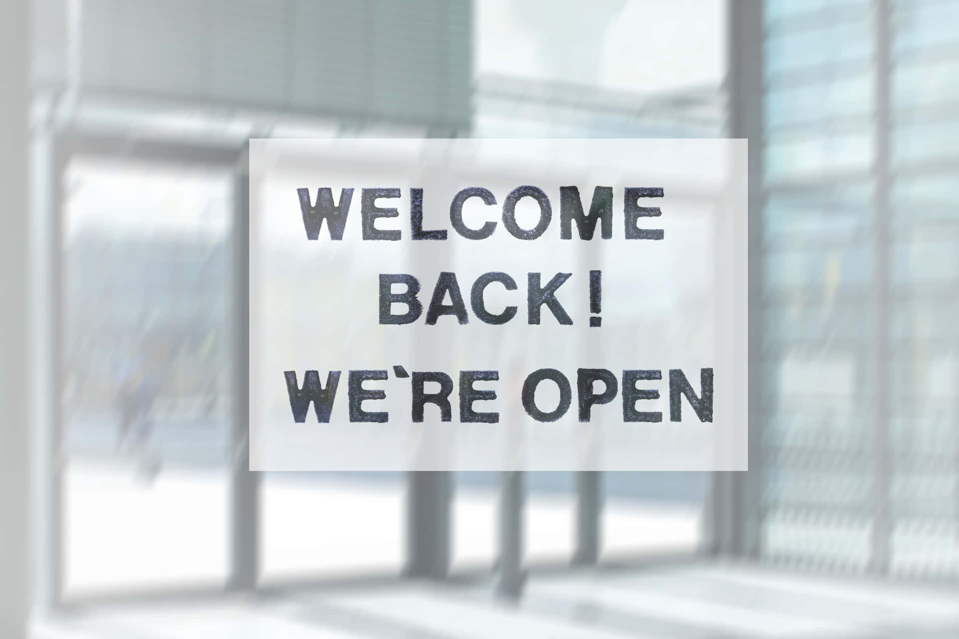  壁紙 — 玻璃門上寫有「WELCOME BACK! WE'RE OPEN」的歡迎標誌，背景是模糊的現代建築。