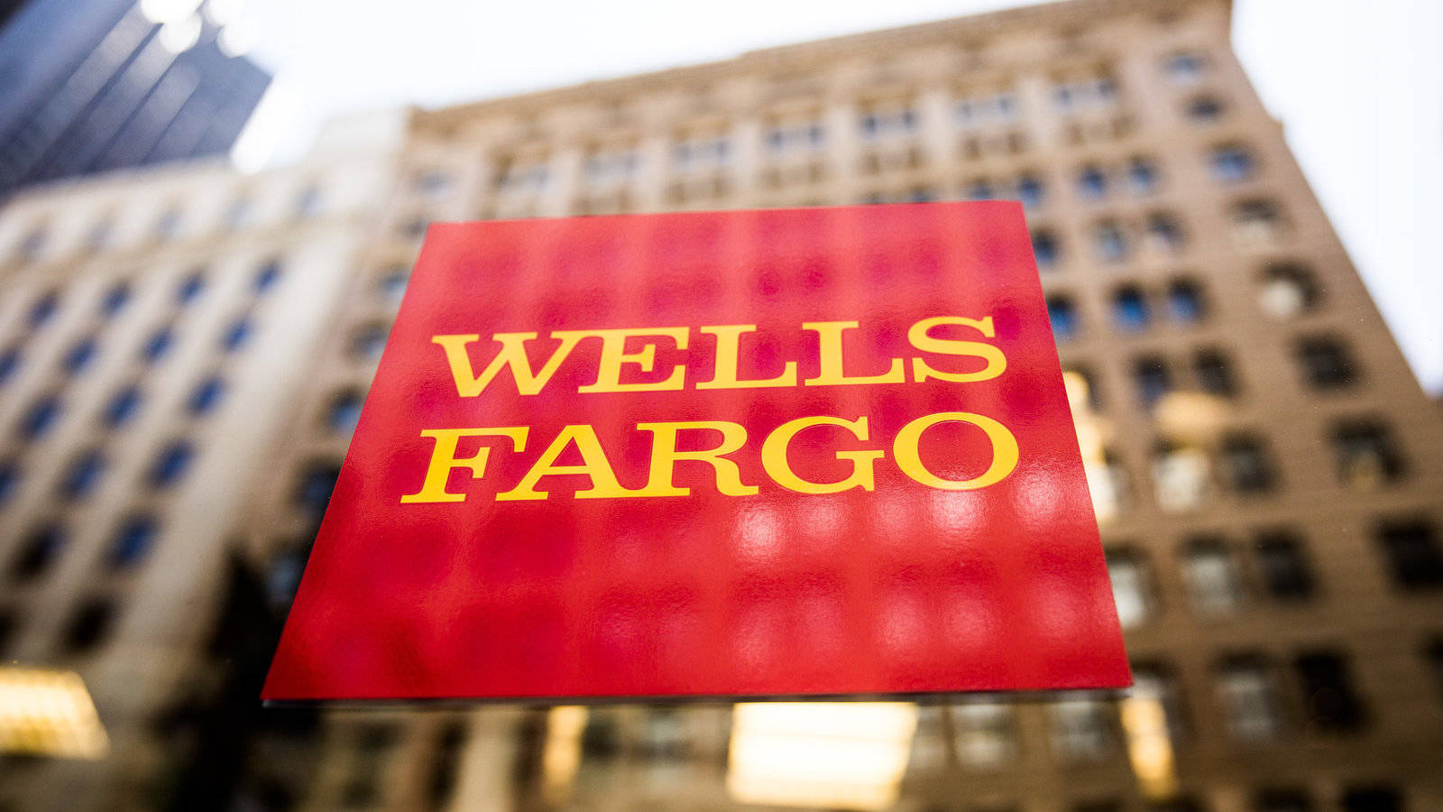 玻璃上的紅色 Wells Fargo 標誌，背後是模糊的城市建築。