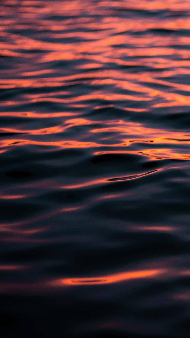黑暗的水面漣漪閃爍著橙色和紅色的夕陽倒影。
