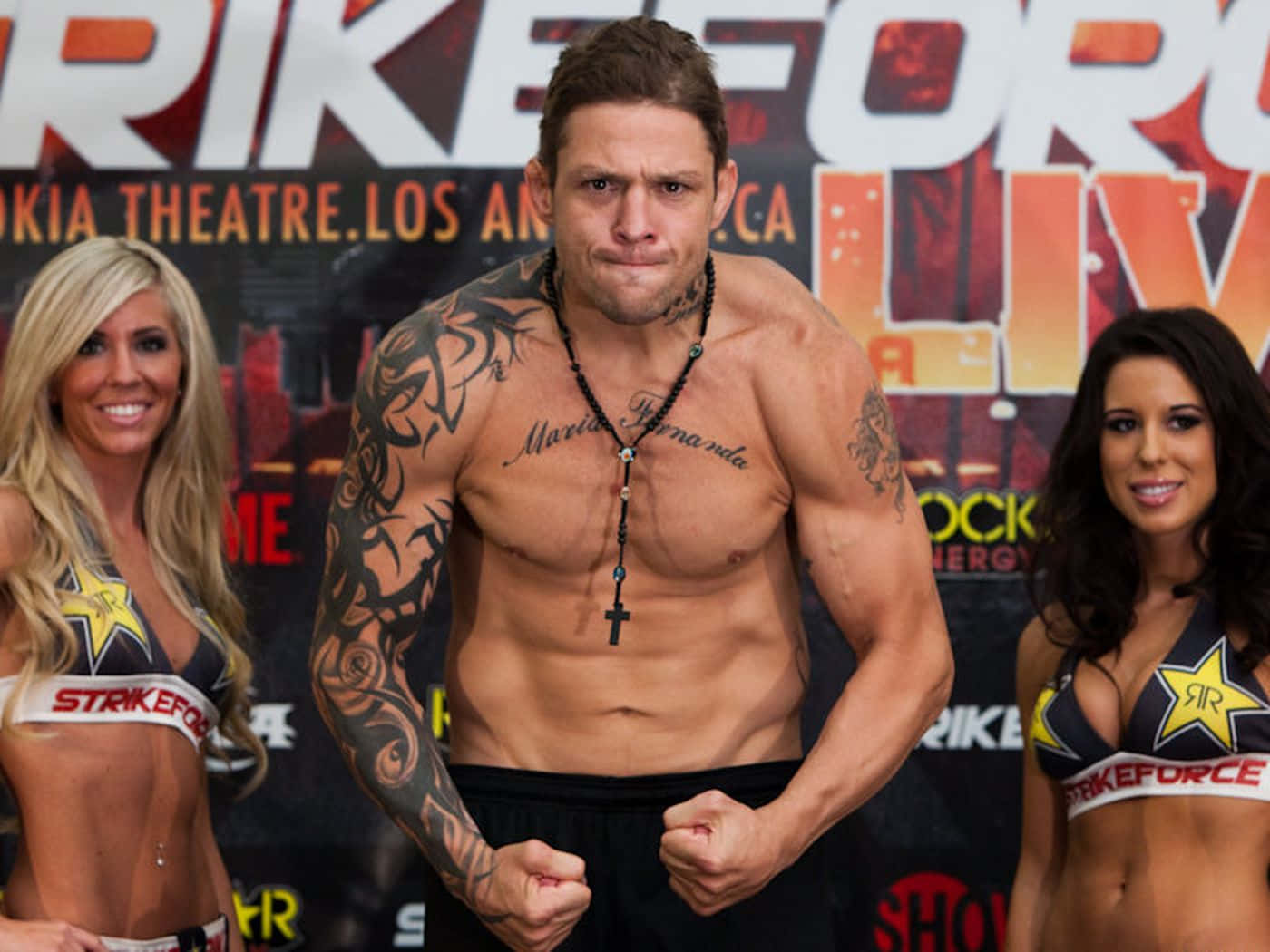  壁紙 — 一位紋身男拳手在Strikeforce稱重儀式上，在兩位微笑的舉牌女郎旁用力繃緊肌肉。