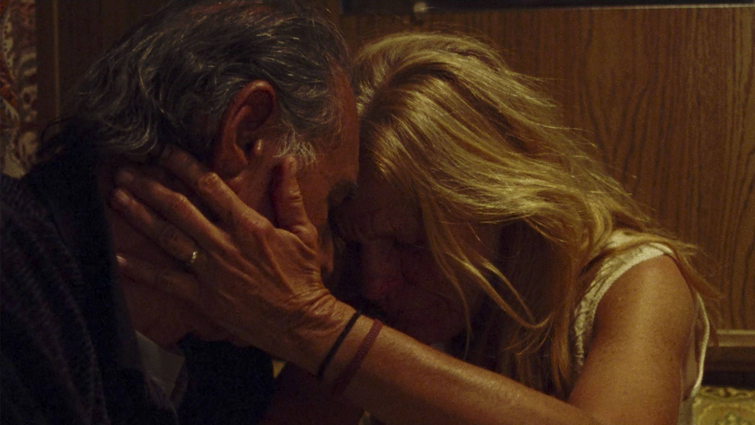 Wes Studi 與 Dale Dickey 壁紙 — 一個親密的特寫鏡頭，金髮女子在溫暖的木質房間裡溫柔地擁抱一位年長男子。