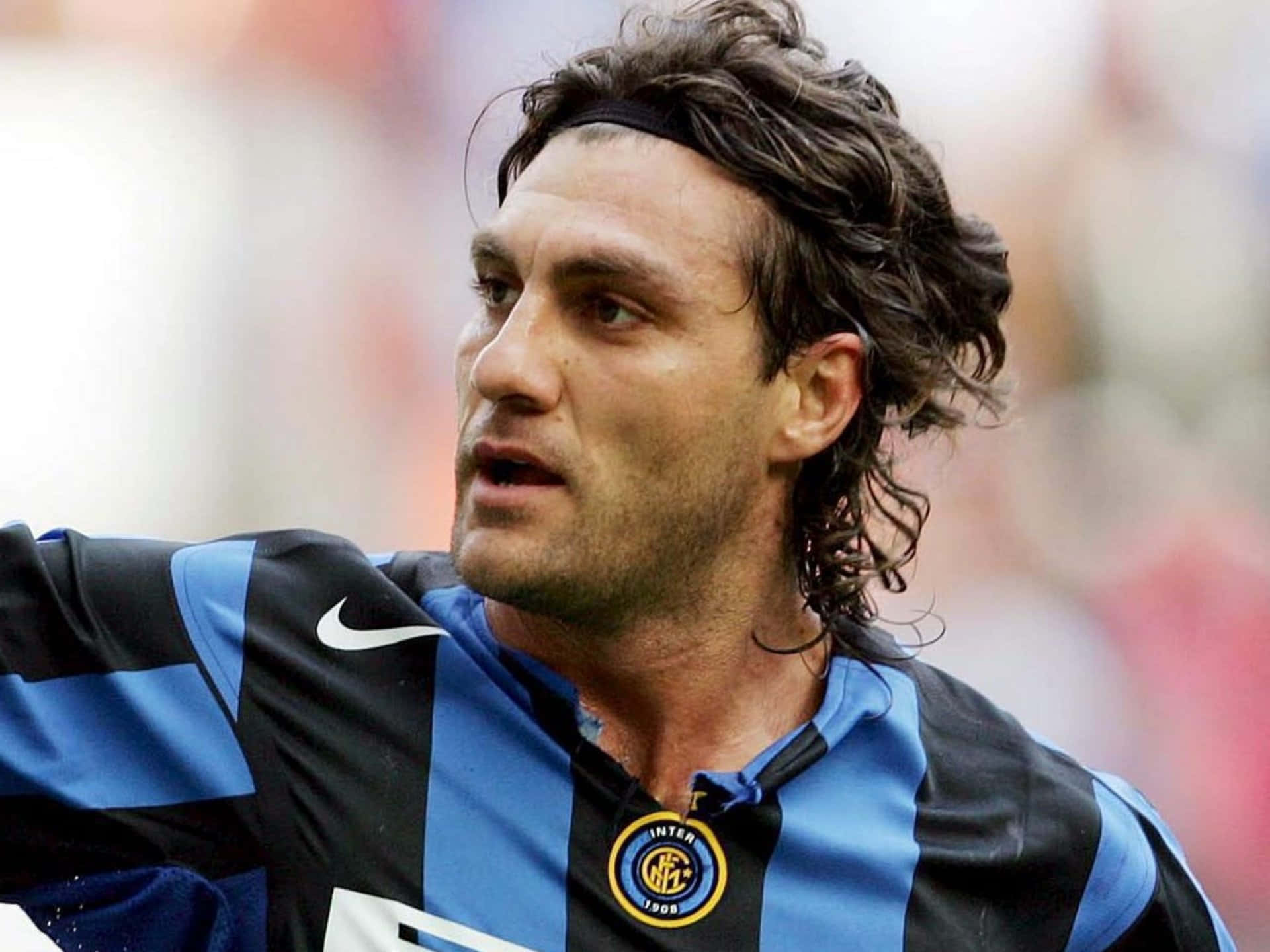 Western United Christian Vieri 壁紙 — 一位專注的足球運動員，身穿藍黑條紋球衣，頭戴頭帶，在比賽中專注地向前看。