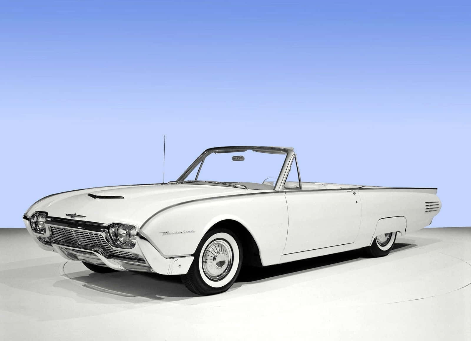Ford Thunderbird 桌布 壁紙 — 一架純白色的1960年代福特雷鳥開篷車在攝影棚燈光下閃閃發光，背景為藍色漸變。