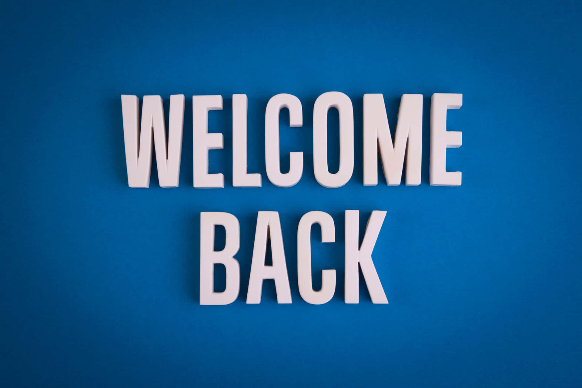  壁紙 — 白色3D字母拼出WELCOME BACK，在純藍色背景上突出顯示。