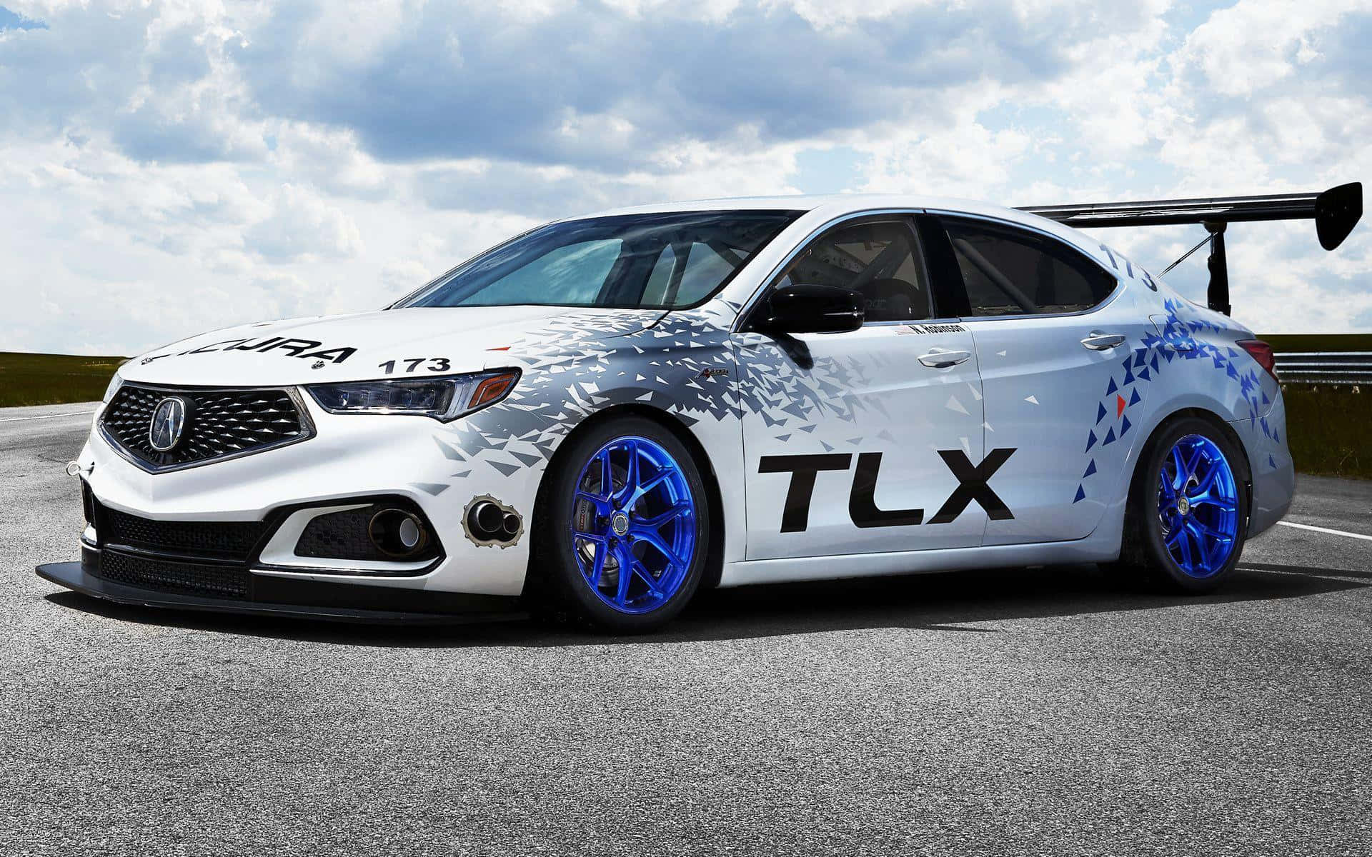 Acura Tlx 桌布 壁紙 — 一輛白色Acura TLX賽車，配備藍色輪圈和幾何圖案貼花，在多雲的天空下於賽道上飛馳。