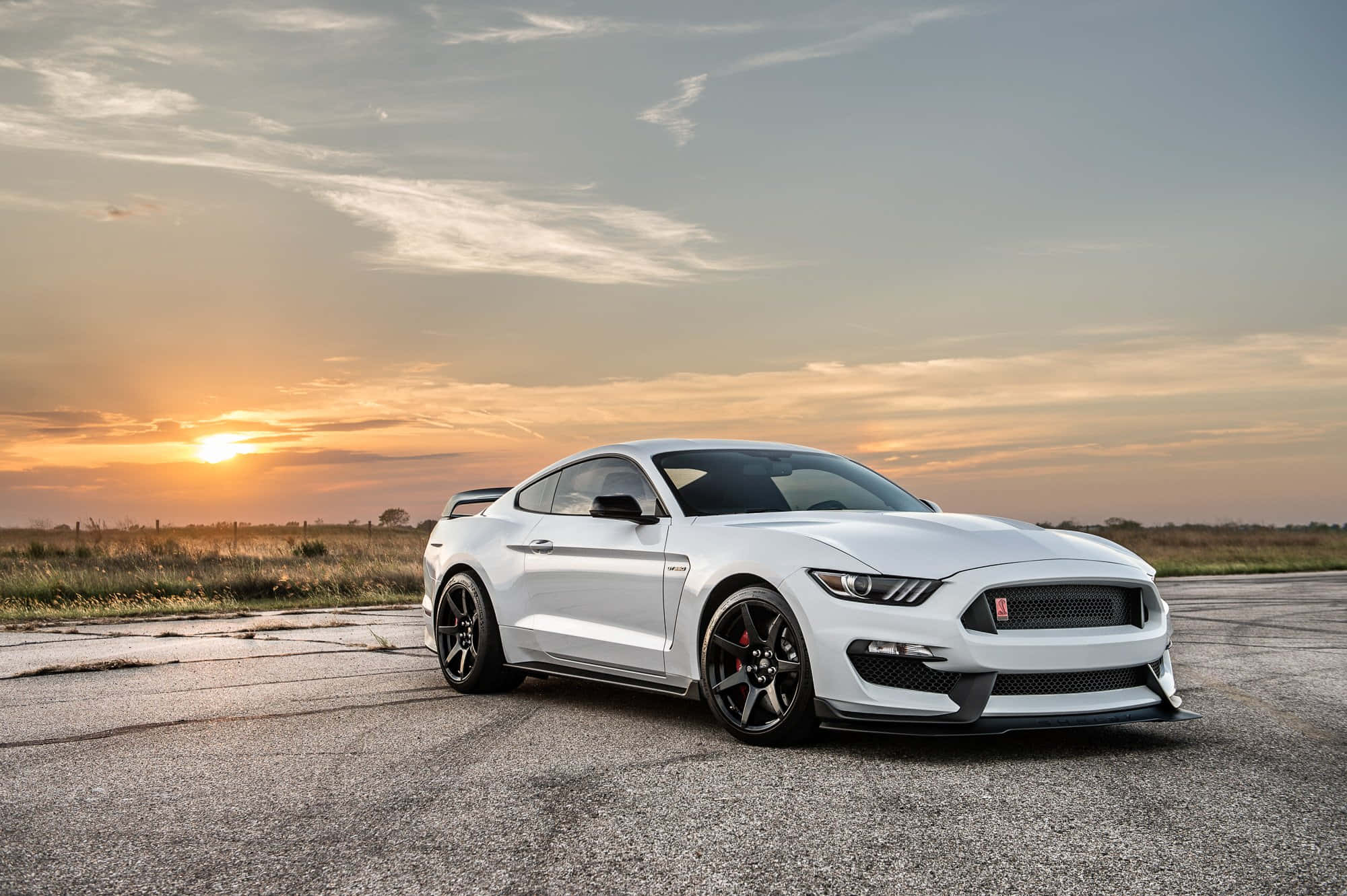 Ford Mustang Gt350r 桌布 壁紙 — 一架白色福特野馬跑車停泊在龜裂的瀝青路上，背景是金色夕陽天空與散落的雲朵。