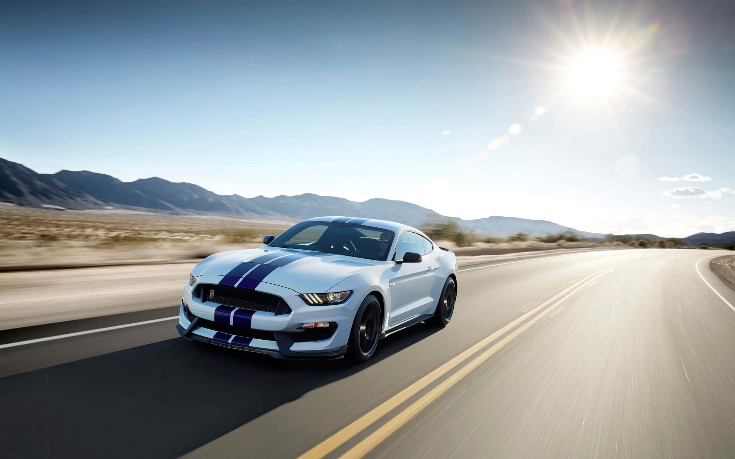 Ford Mustang Shelby Gt350 桌布 壁紙 — 一輛帶有藍色賽車條紋的白色福特野馬在明亮的陽光下，以山脈為背景，在沙漠公路上疾馳。