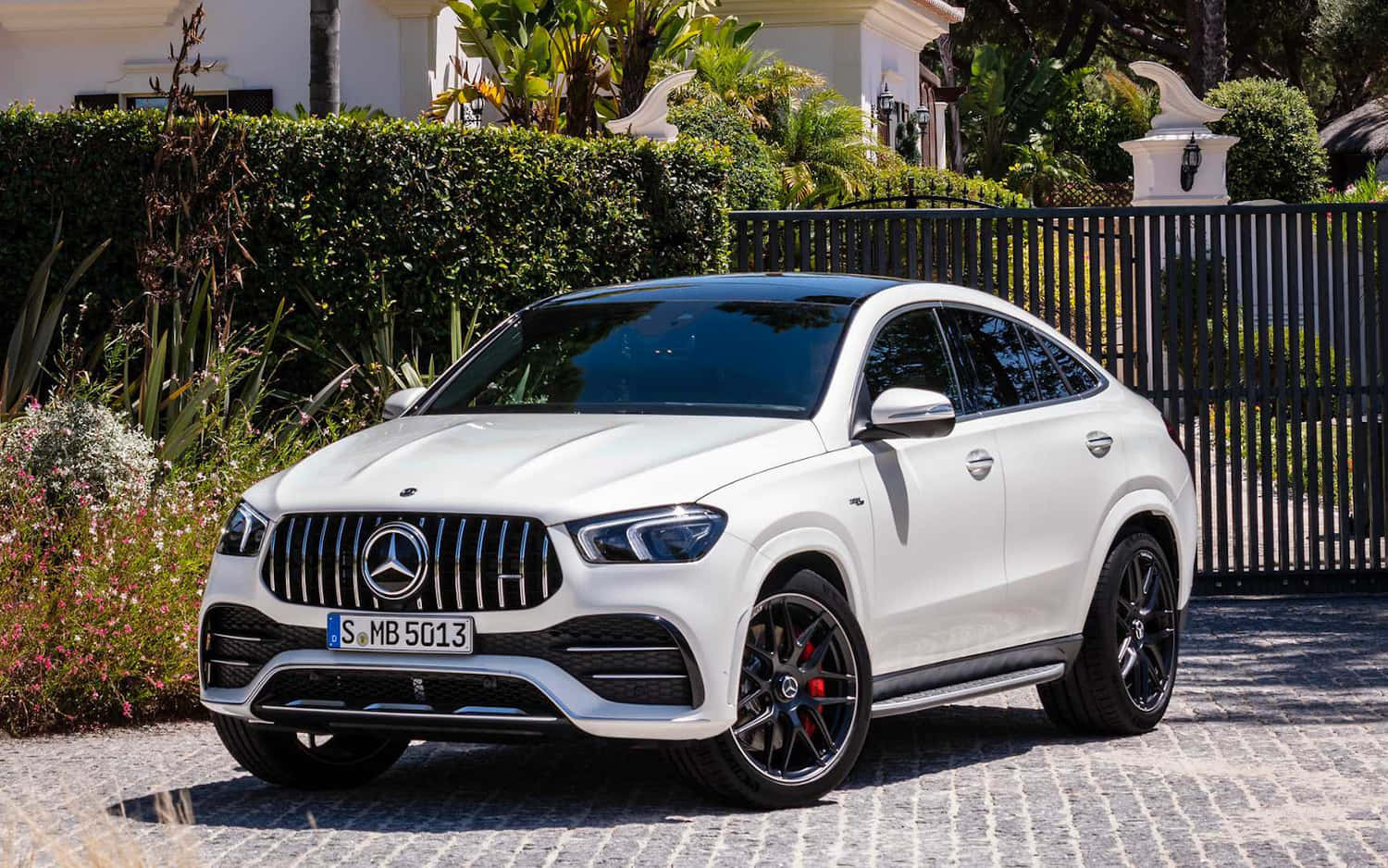 Mercedes Benz Gle-class 桌布 壁紙 — 一架完美無瑕的白色 Mercedes-AMG GLE Coupe 停泊在陽光普照的鵝卵石車道上，旁邊是修剪整齊的樹籬和黑色鍛鐵圍欄。