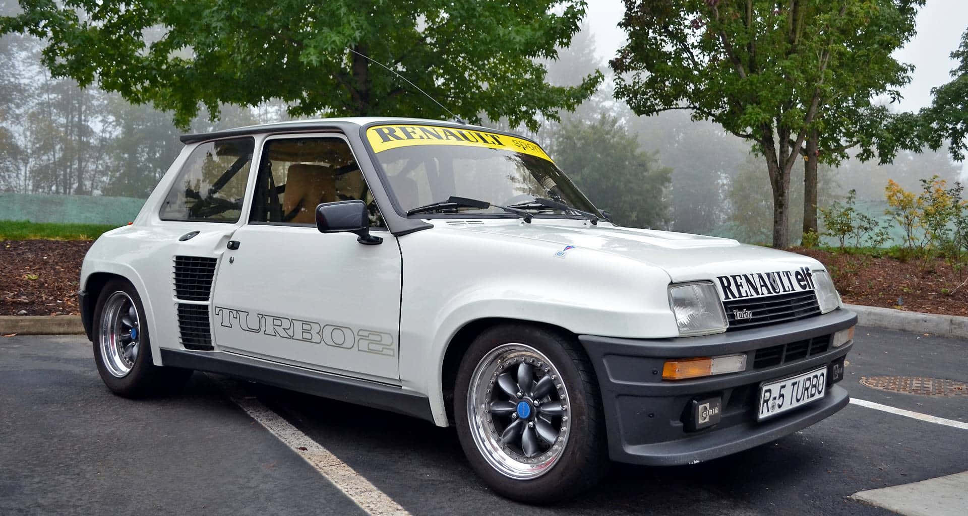 Renault 5 Turbo 桌布 壁紙 — 一輛白色雷諾5 Turbo 2拉力賽車停泊在霧氣瀰漫、樹木成排的停車場，背景同樣霧濛濛。