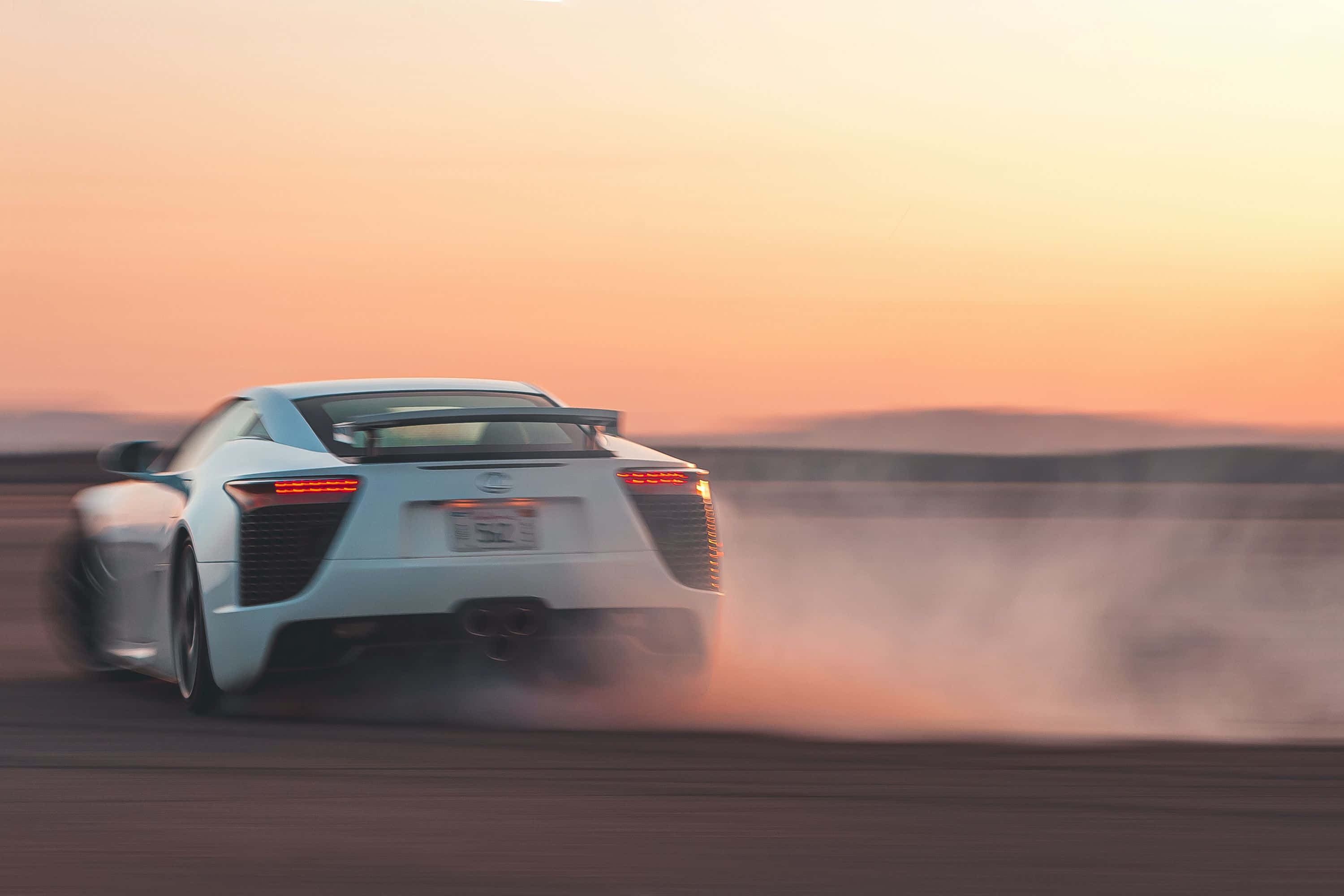 Lexus Lfa 桌布 壁紙 — 一輛白色跑車在日落時分在沙漠賽道上飄移，揚起塵土，天空呈現溫暖的橙色。