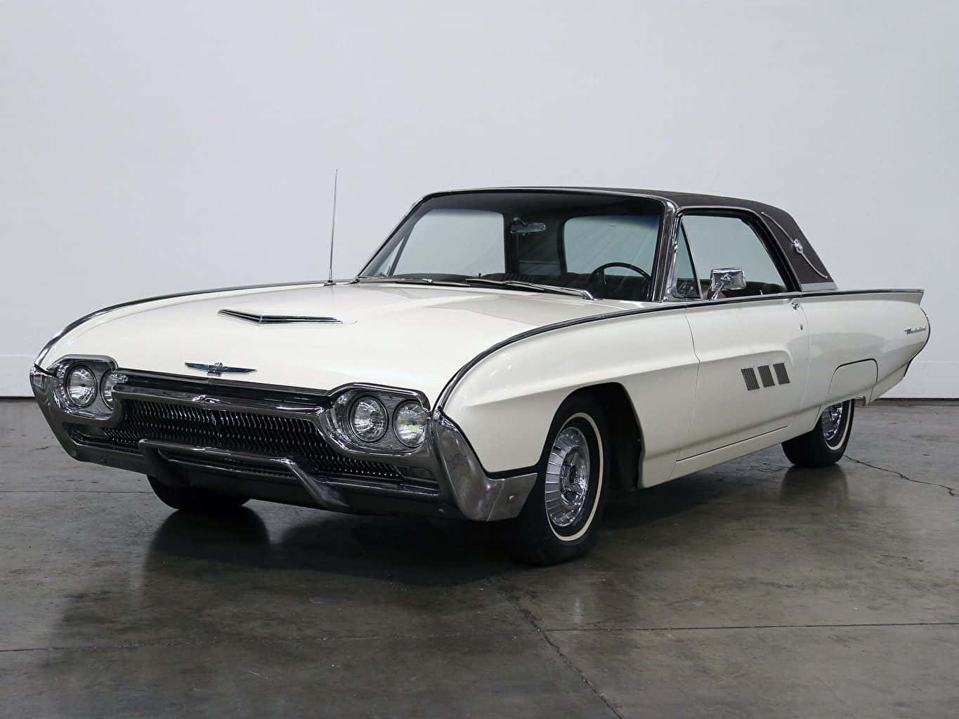 Ford Thunderbird 桌布 壁紙 — 一架純白色的1960年代福特雷鳥開篷車，配備黑色車頂和鍍鉻裝飾，矗立在簡約的攝影棚空間中。