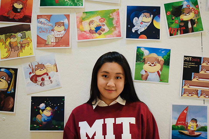 年輕女子穿著紅色MIT運動衫在卡通藝術牆前微笑。