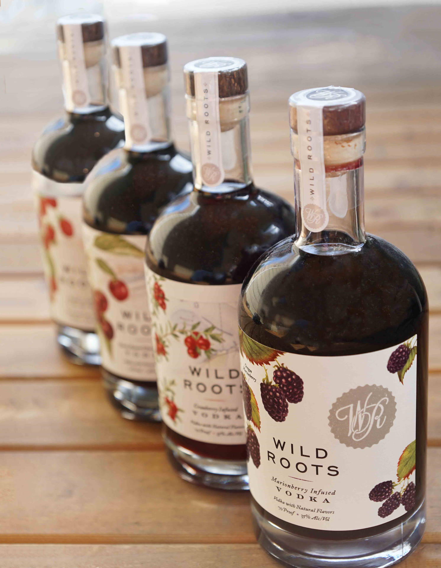 四瓶帶有莓果標籤的Wild Roots伏特加在木桌上。