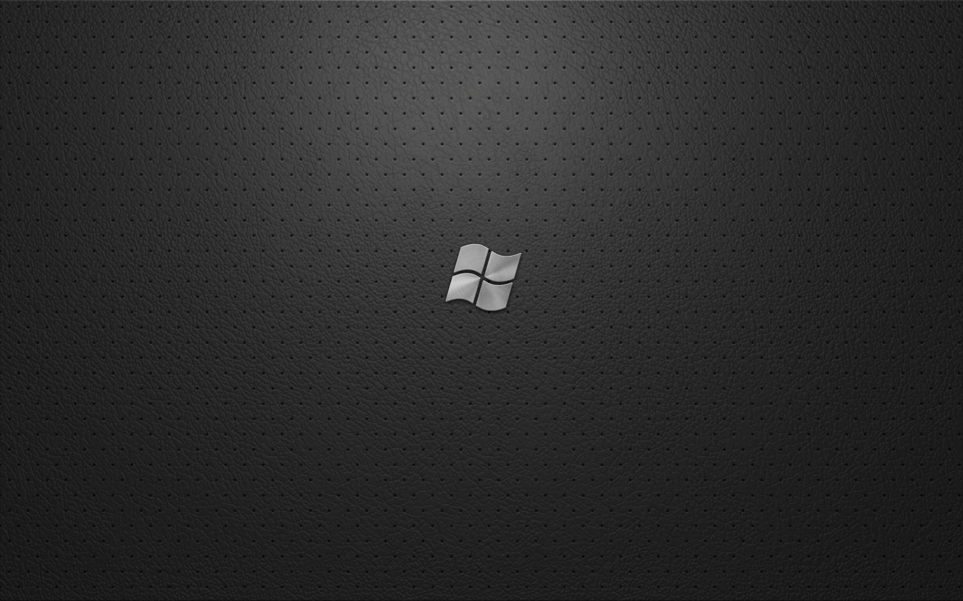 單色 Windows 10 壁紙 — 一個時尚的銀色Windows標誌居中在深色穿孔皮革狀表面上，帶有柔和漸變照明。
