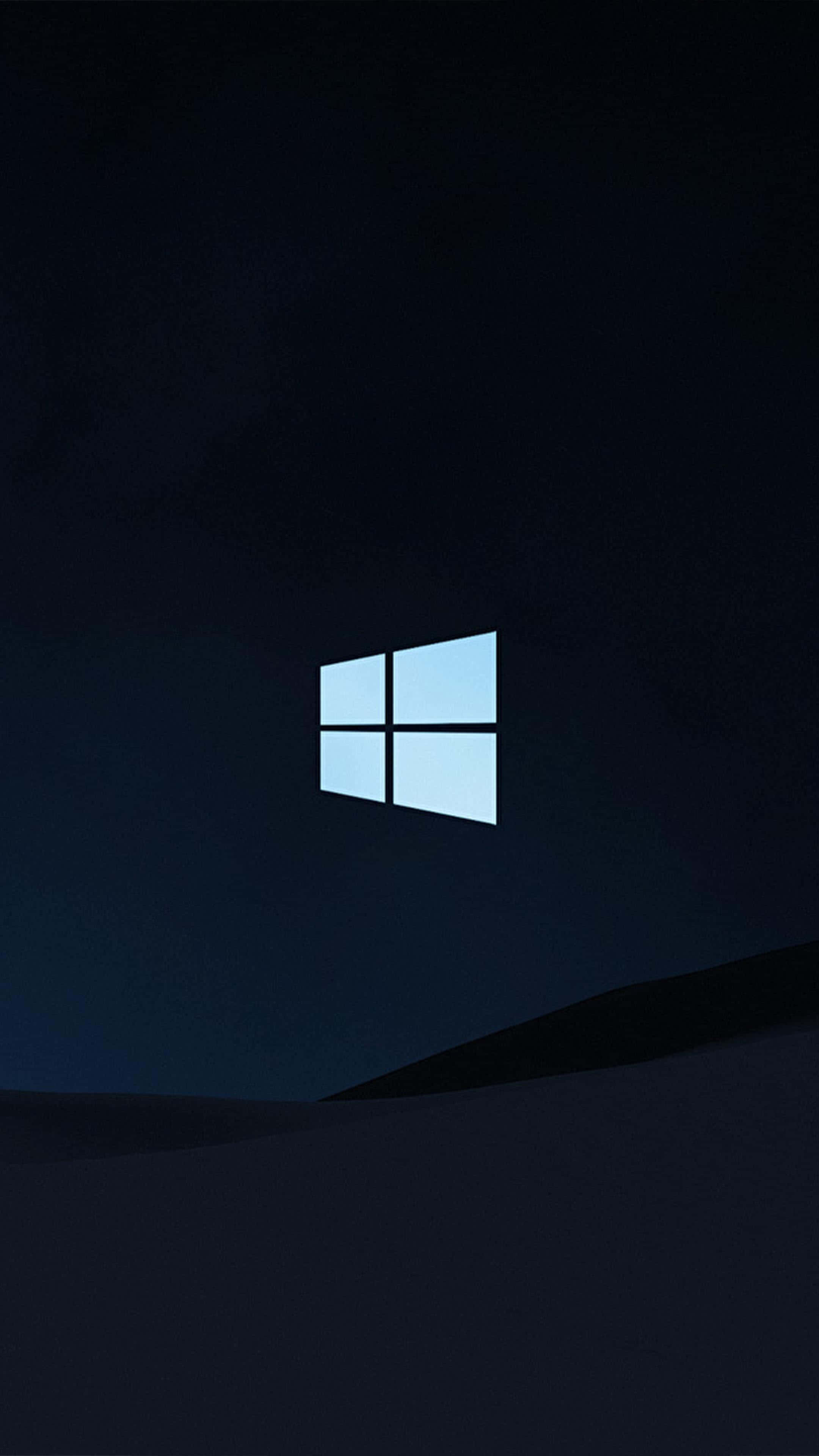 Windows 10 上的寧靜日落風景 壁紙 — 一個發光的藍色Windows標誌漂浮在黑暗的夜空中，位於一個陰影籠罩的山丘之上。