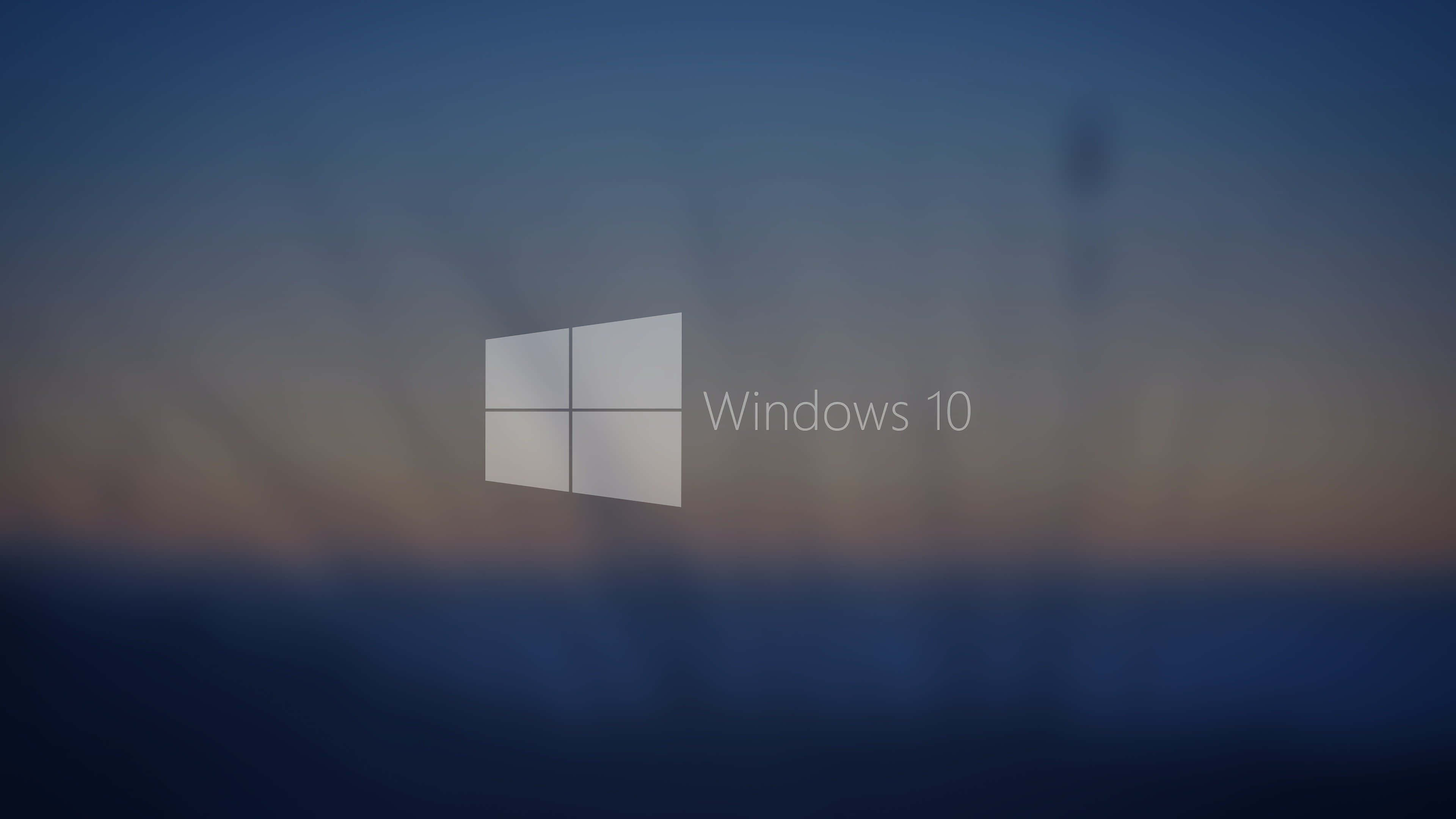 Windows 10 桌面創新 壁紙 — Windows 10 標誌居中，背景為模糊的暮色天空，帶有柔和的藍色和橙色漸變。