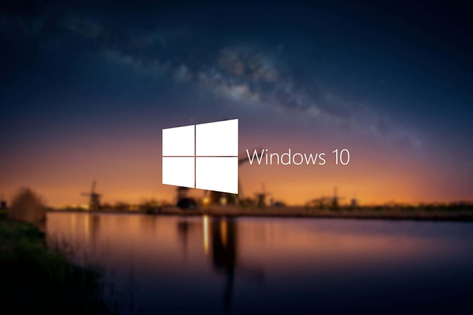 Windows 10 標誌在暮色景觀上，有風車和水面倒影。