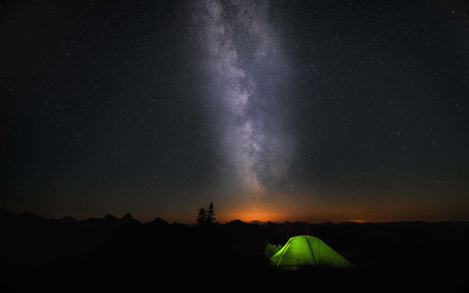 一個發光的綠色帳篷在星空下，銀河在山脈上方。