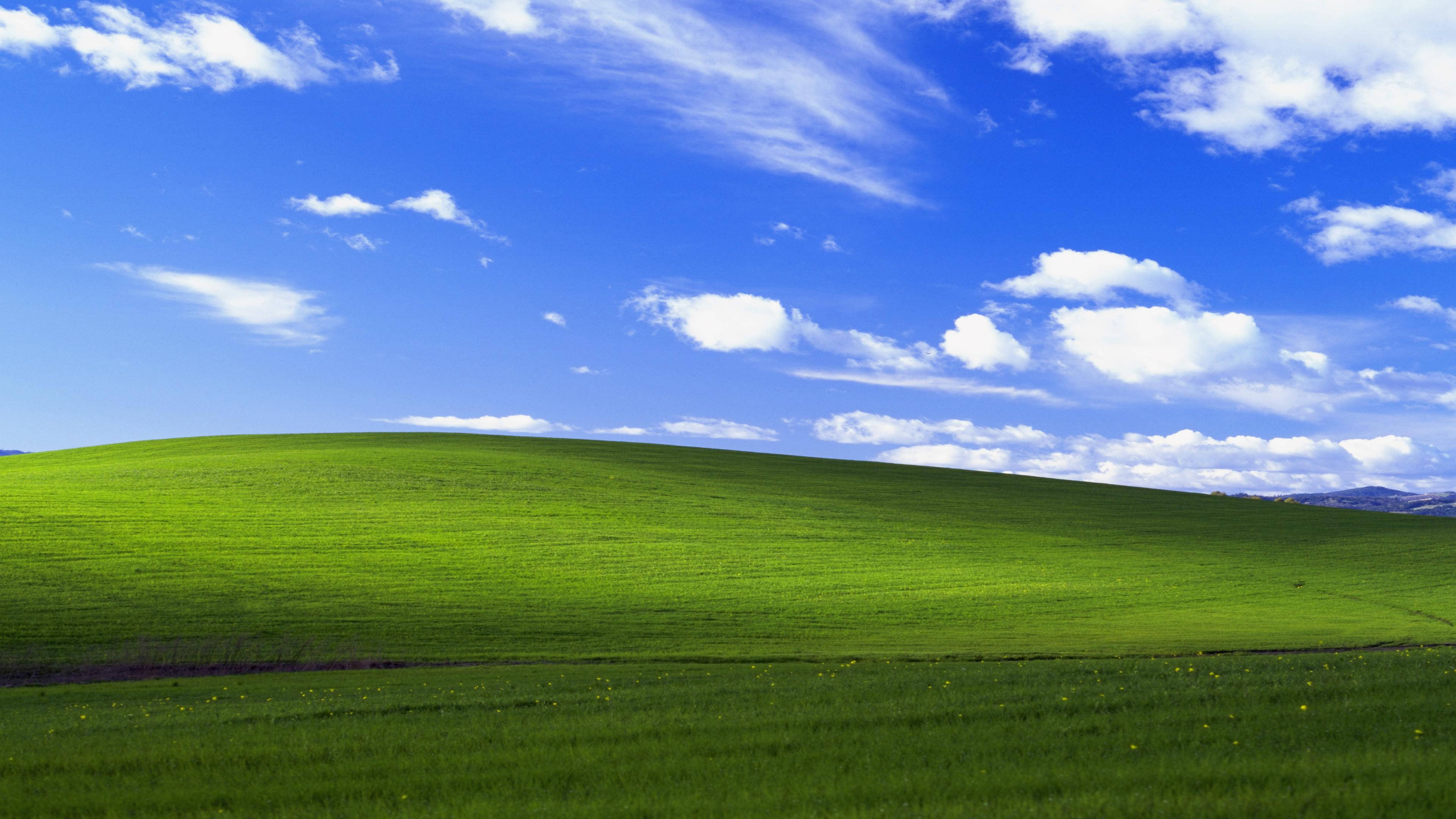 Windows 10 高清 Bliss 壁紙 — 廣闊起伏的綠色山丘在明亮的藍天下延伸，點綴著蓬鬆的白雲。