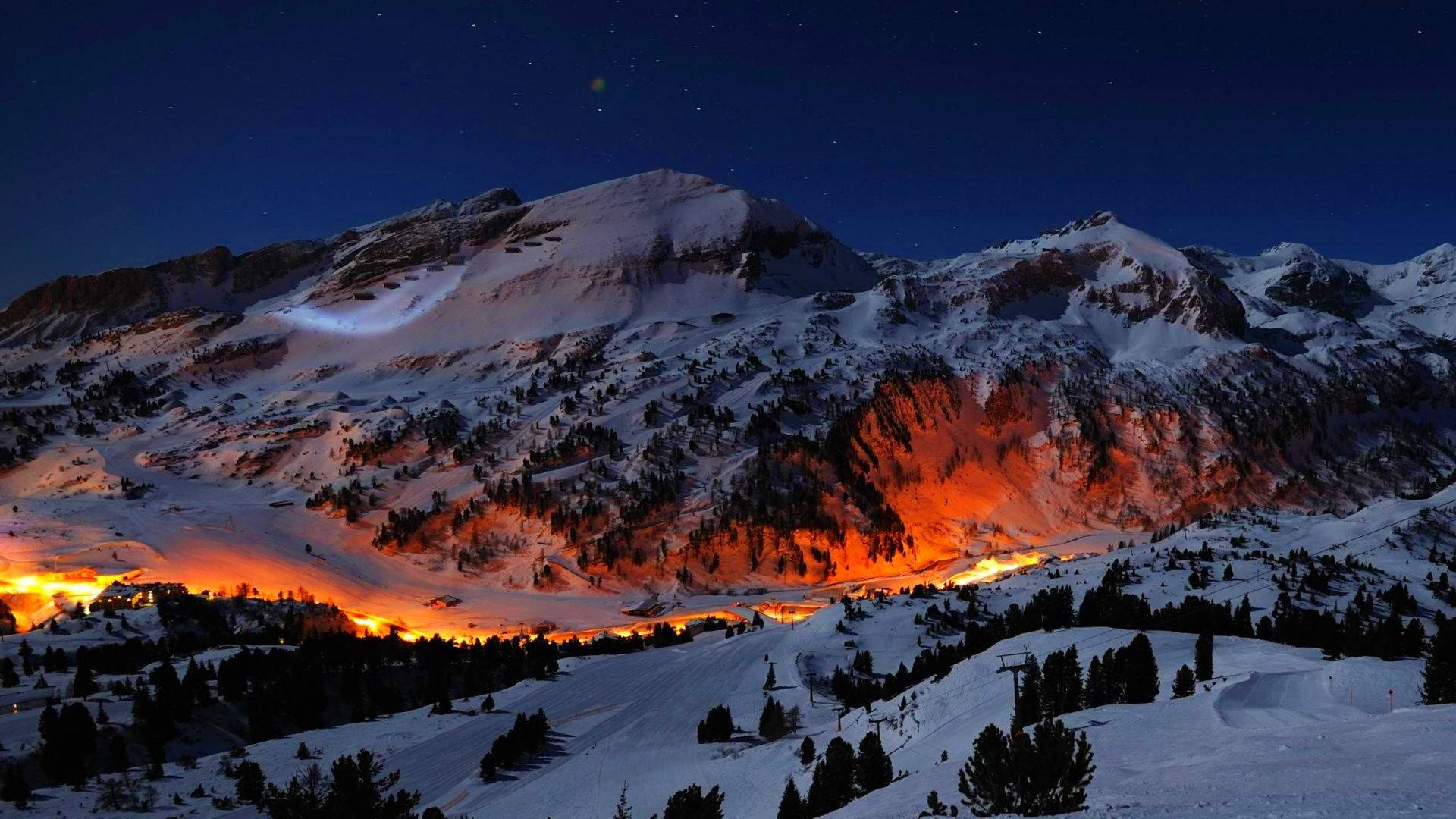 Windows 10 高清冰川山脈 壁紙 — 積雪的山峰在繁星點點的夜空下閃耀著火熱的橙色光芒。