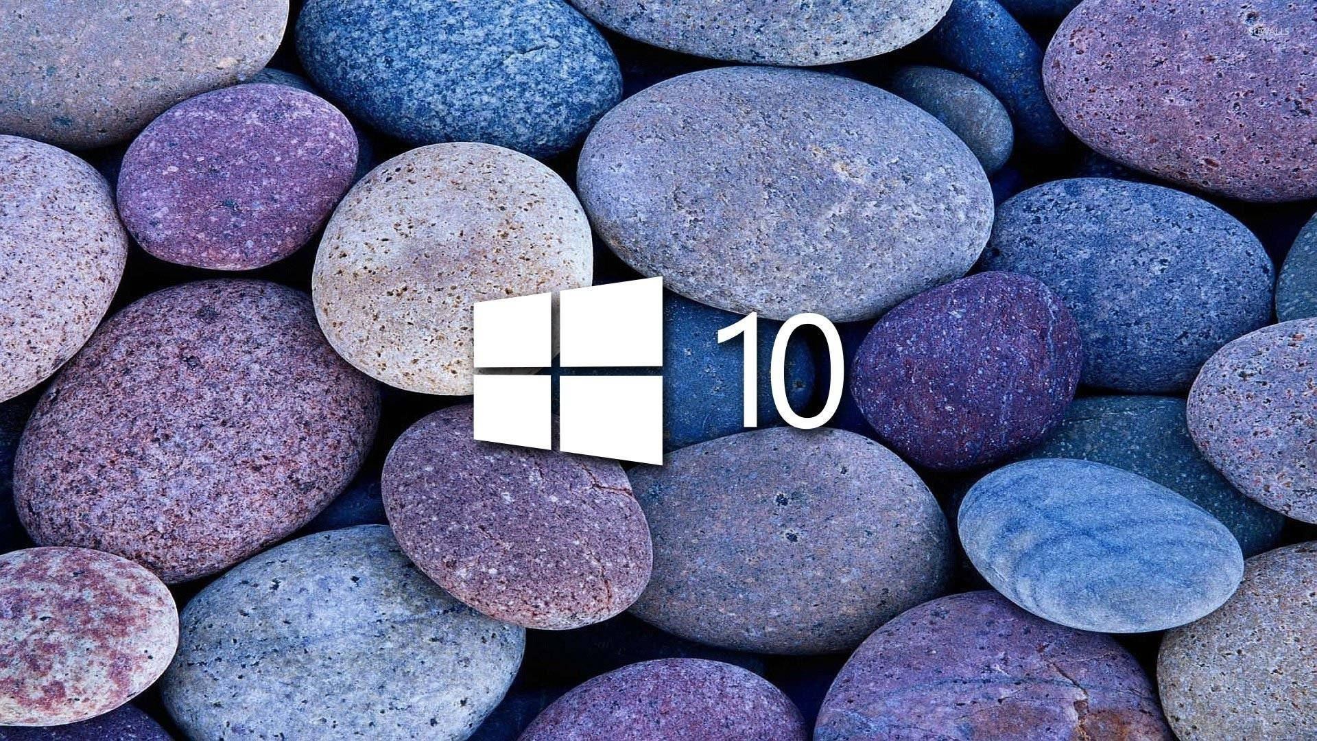 Windows 10 高清冷色石堆 壁紙 — Windows 10 標誌居中放置在平滑的多色河石床上，顏色有藍色、紫色和灰色。