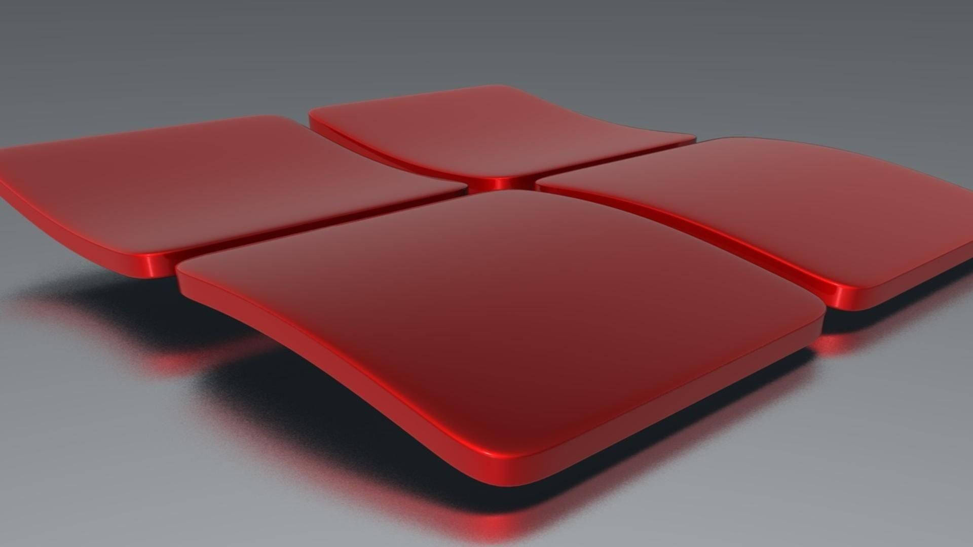 Windows 11 3D 紅色標誌 壁紙 — 四個光澤紅色弧形面板以十字形排列在灰色表面上，帶有柔和陰影。