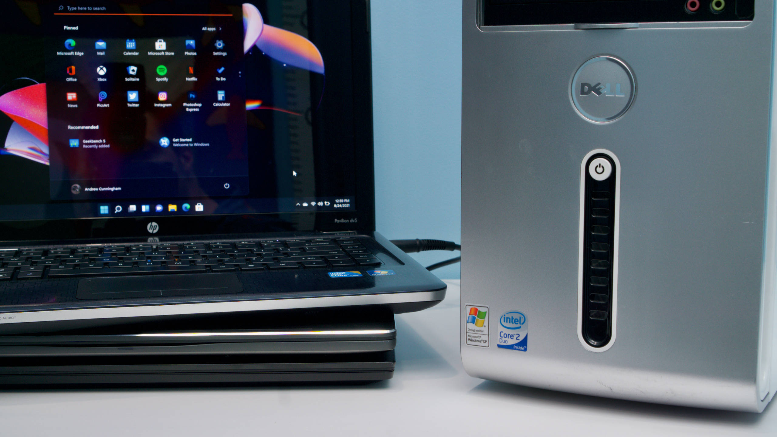 Windows 11 戴爾與惠普 壁紙 — 一部 Dell 桌面主機和一部 HP 手提電腦並排放置在白色表面上，螢幕上顯示 Windows 開始功能表。