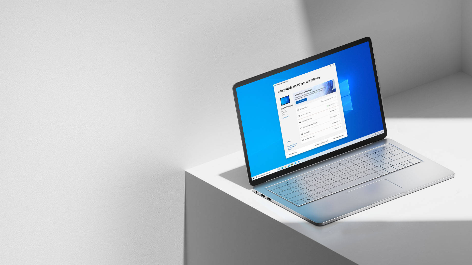 Windows 11 白色角落 壁紙 — 一部纖薄的銀色手提電腦在簡約的白色邊緣上打開，在明亮的攝影棚燈光下顯示 Windows 設定畫面。