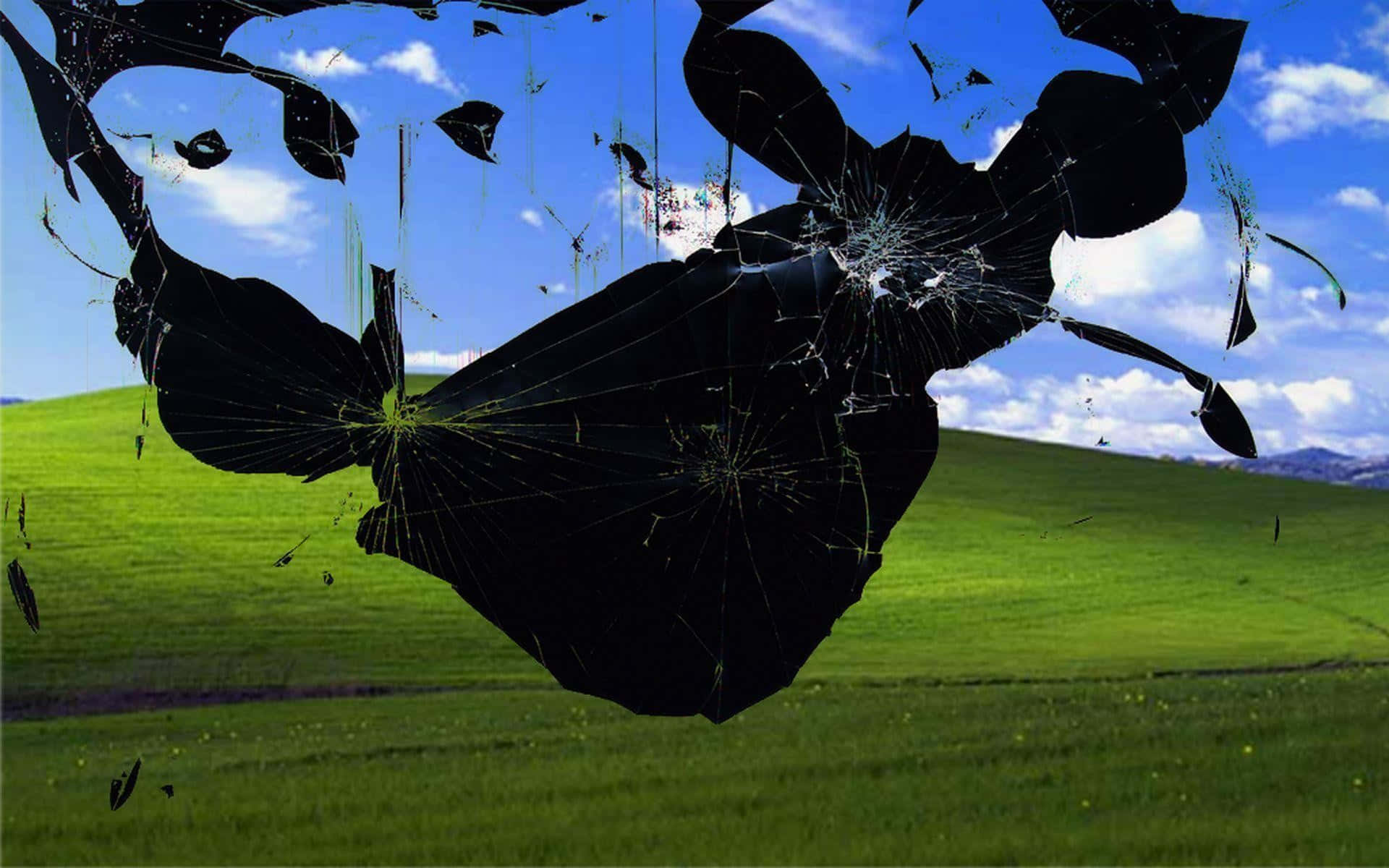 時尚 Windows 桌面背景 壁紙 — 一塊破碎的黑色玻璃覆蓋層在經典的綠色起伏山丘上裂開，上方是明亮的藍天和蓬鬆的雲朵。