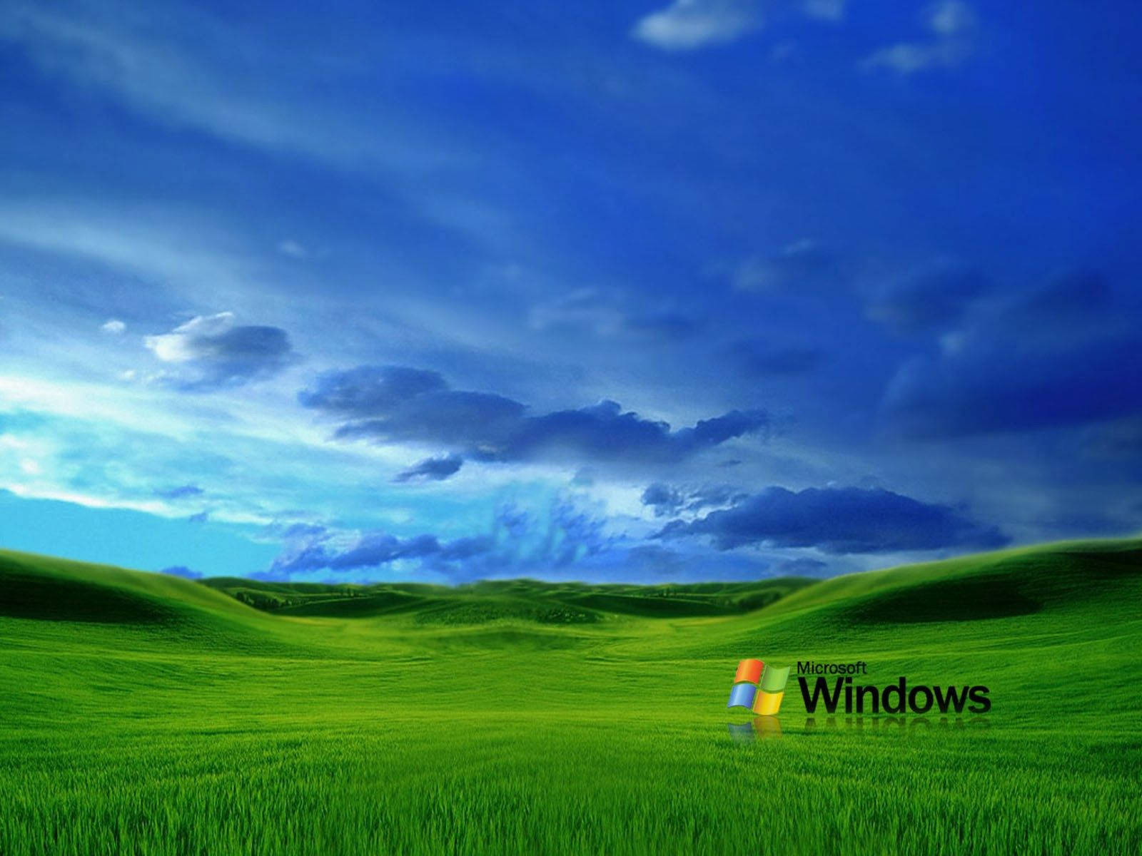 Windows Vista 預設桌面 壁紙 — 廣闊起伏的綠色山丘在戲劇性的藍天下延伸，點綴著散落的雲朵，前景是Windows標誌。