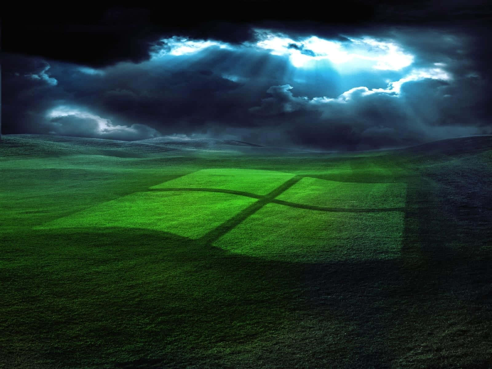 欣賞 Windows XP 的經典設計與功能 壁紙 — 暴風雨的天空帶著戲劇性的光束照亮了一片廣闊的綠色田野，上面有一個發光的Windows標誌。