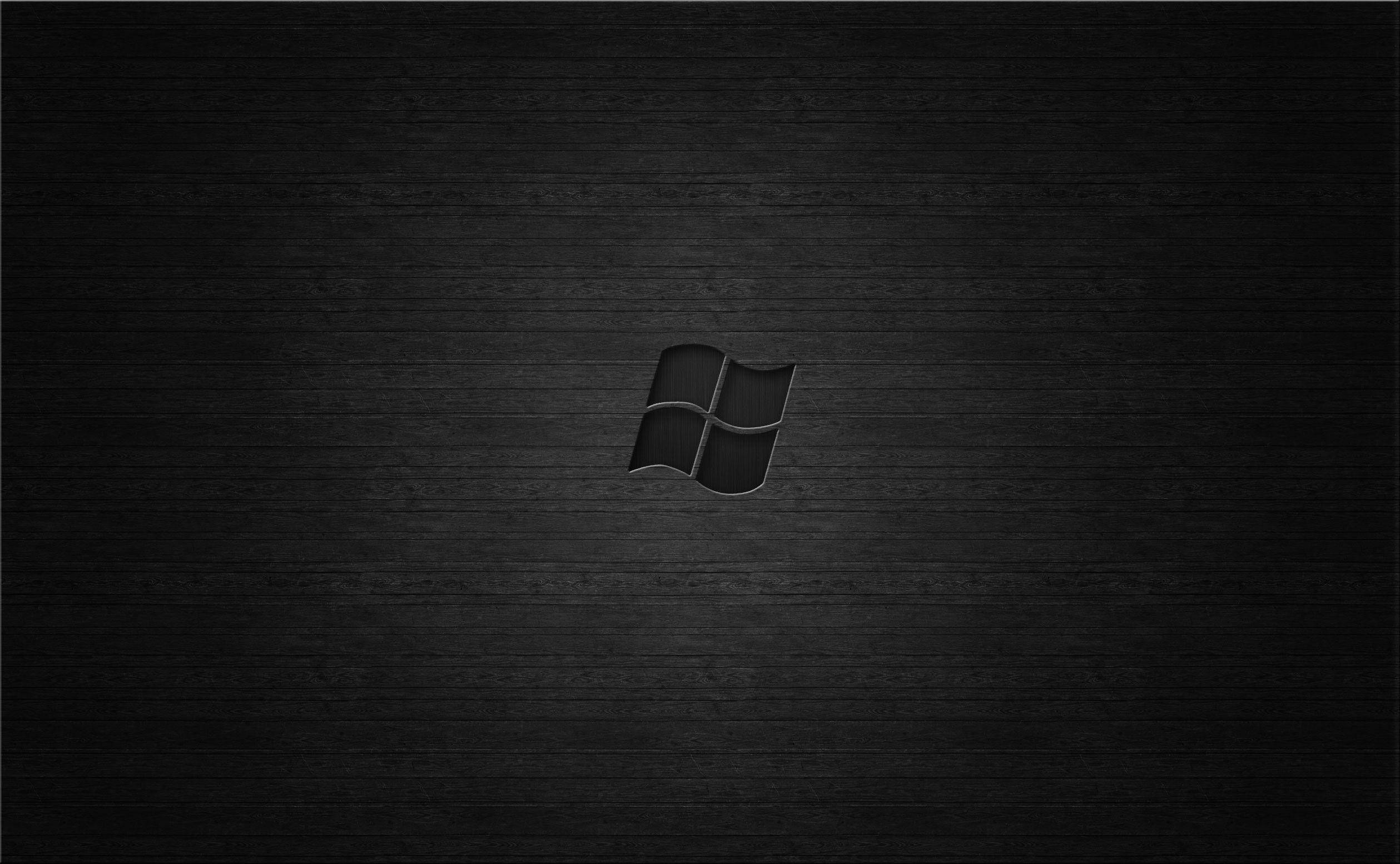 壓印深色Windows標誌 壁紙 — 一個極簡黑色Windows標誌居中於深色紋理木質表面，帶有柔和燈光。