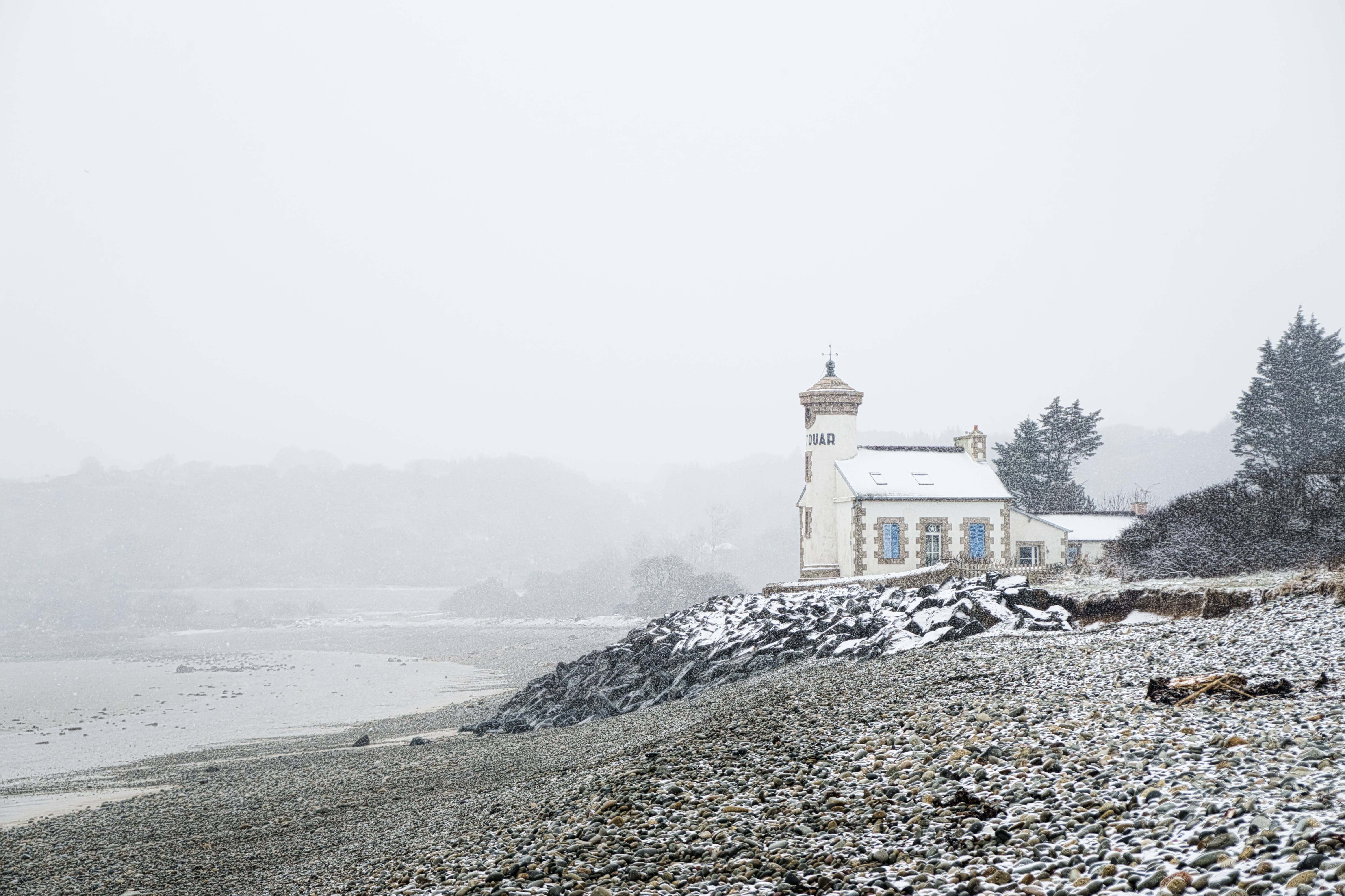 Windows 冬日海濱小屋 壁紙 — 一座被雪覆蓋的燈塔孤獨地矗立在岩石海岸上，伴隨著冬季暴風雪和灰暗的天空。