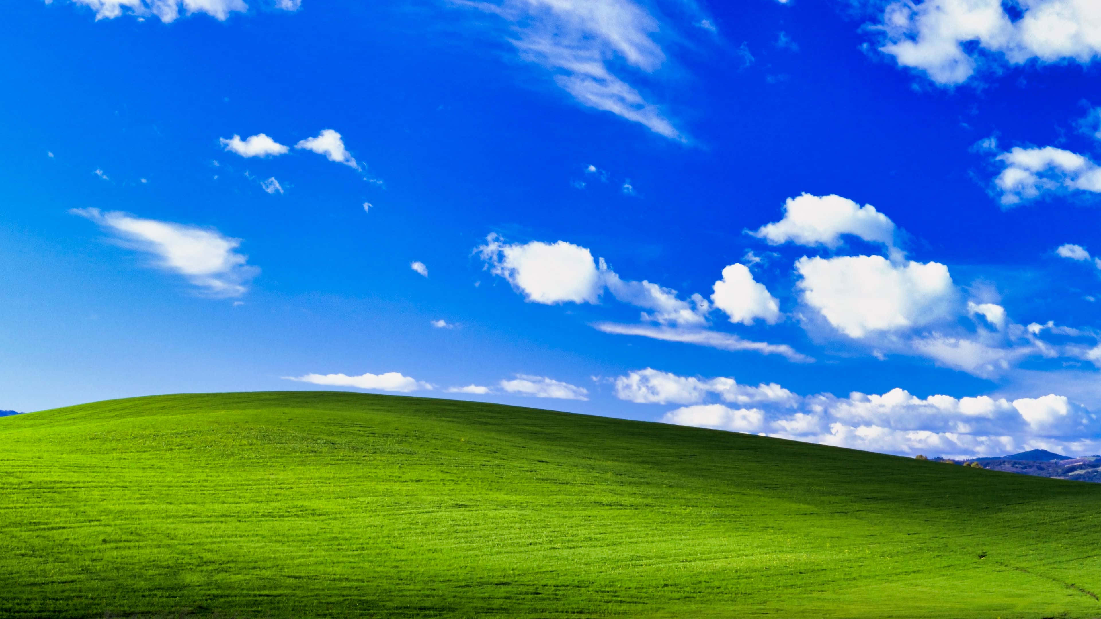 Windows 預設背景 壁紙 — 廣闊起伏的綠色山丘，在明亮的藍天下點綴著蓬鬆的白雲。