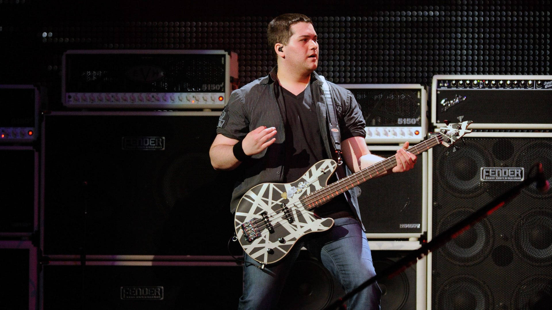 Wolfgang Van Halen 基音樂器獨奏 壁紙 — 一位貝斯手在舞台上，被Fender擴音器包圍，在明亮的舞台燈光下彈奏一把黑白條紋的貝斯結他。