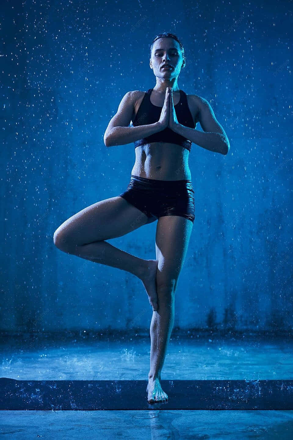  壁紙 — 一名身穿黑色運動服的女性在冷藍光照耀的雨中保持樹式平衡。