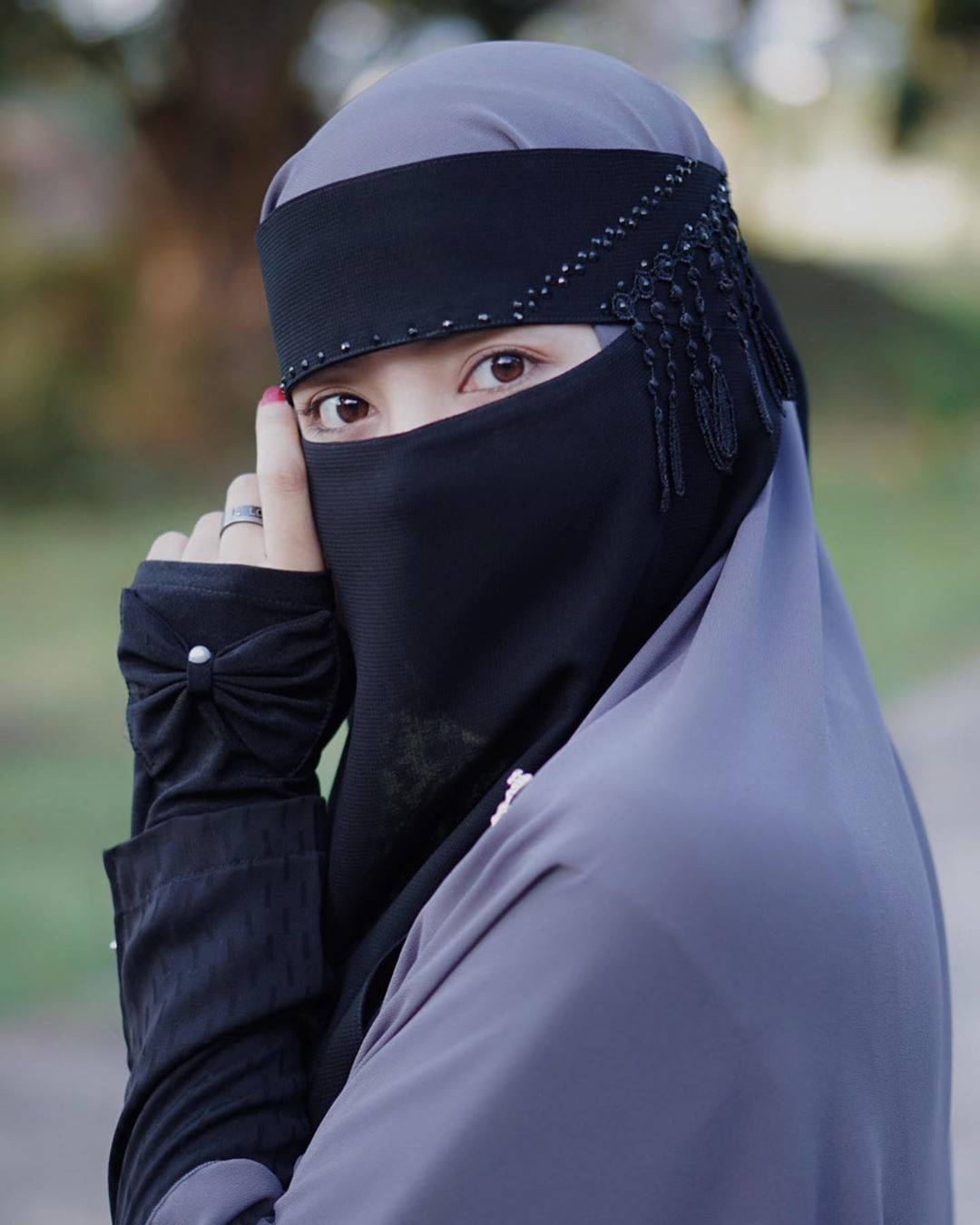 女子身穿黑色尼卡布（帶珠飾邊）和灰色希賈布，在戶外