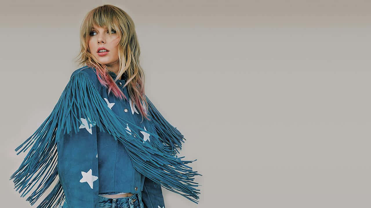 Taylor Swift Lover 桌布 壁紙 — 一位金髮帶有粉紅色挑染的女性，身穿藍色流蘇星星外套，背景為純米色。