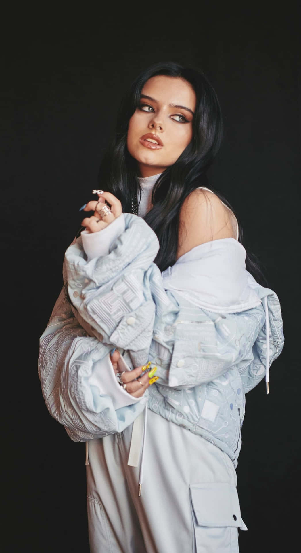  壁紙 — 一位長黑髮女性自信地穿著淺藍色超大外套，在黑色背景前擺姿勢。
