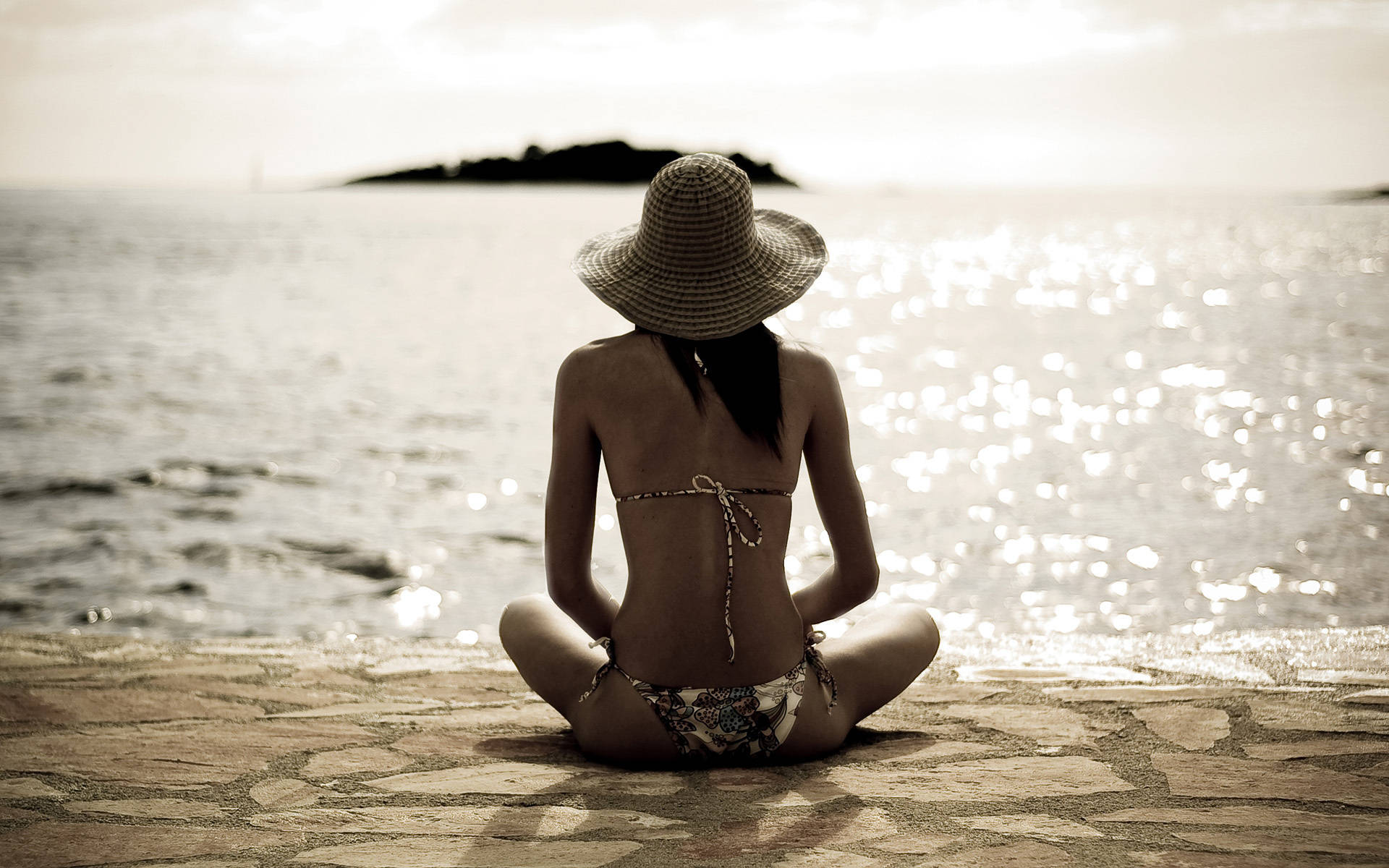 戴草帽的女性在石灘上面對海洋冥想，夕陽西下