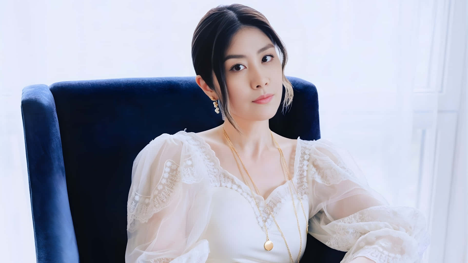  壁紙 — 一位身穿白色蕾絲連衣裙的女性，優雅地坐在一張毛絨藍色椅子上，背景是明亮的窗戶。
