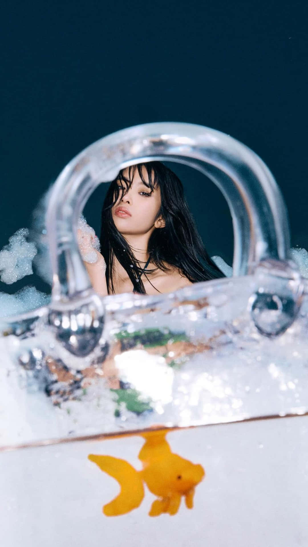  壁紙 — 一位深色頭髮的女性透過浸沒手袋的彎曲手柄凝視，一條金魚在清澈的水中於下方游動。