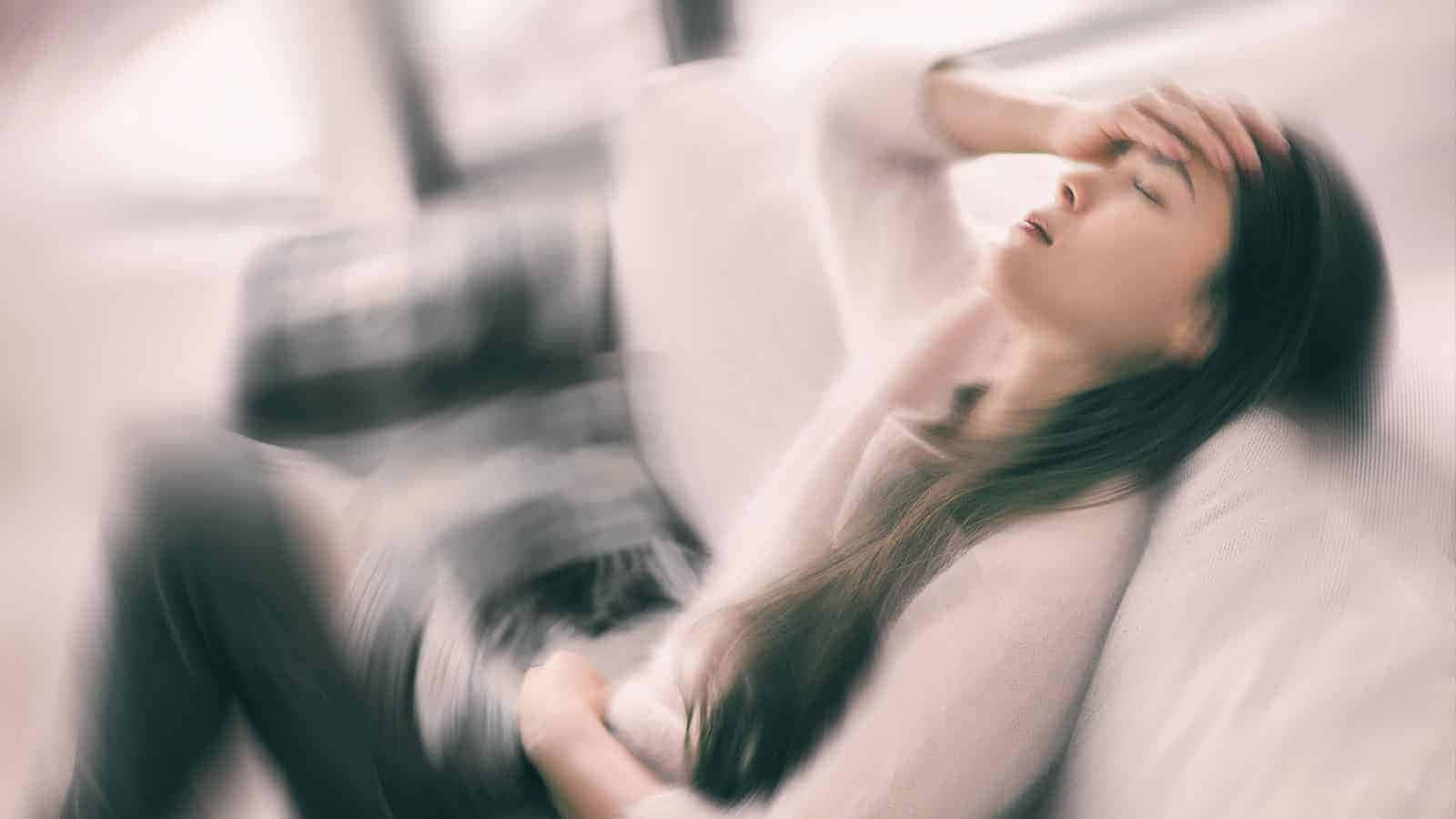  壁紙 — 一位女士將頭靠在枕頭上，閉上眼睛，手放在額頭上，處於柔和模糊的室內環境中。