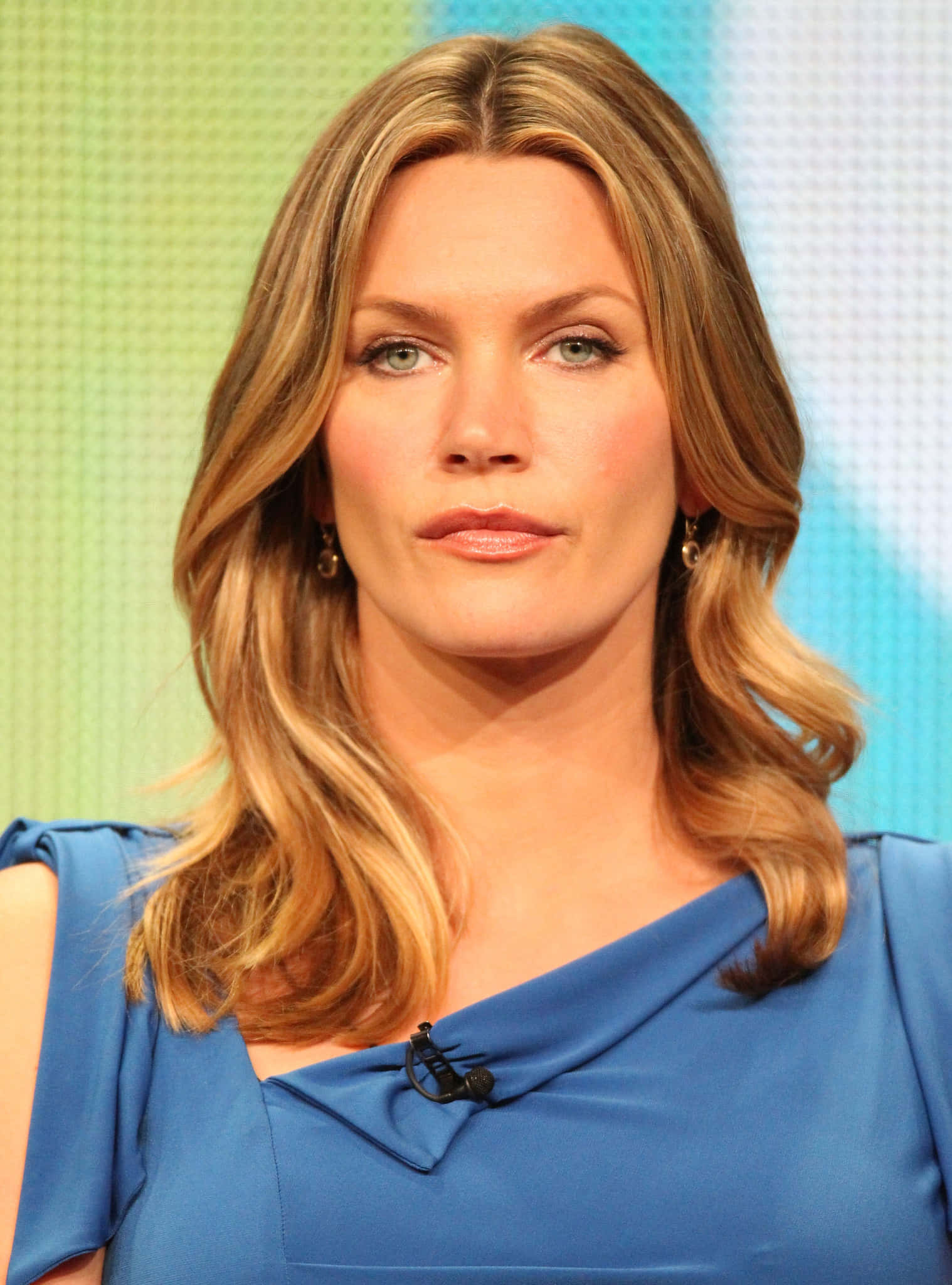 Natasha Henstridge 桌布 壁紙 — 一位金髮波浪長髮、綠眼睛的女性，在彩色網格背景前穿著藍色連衣裙。