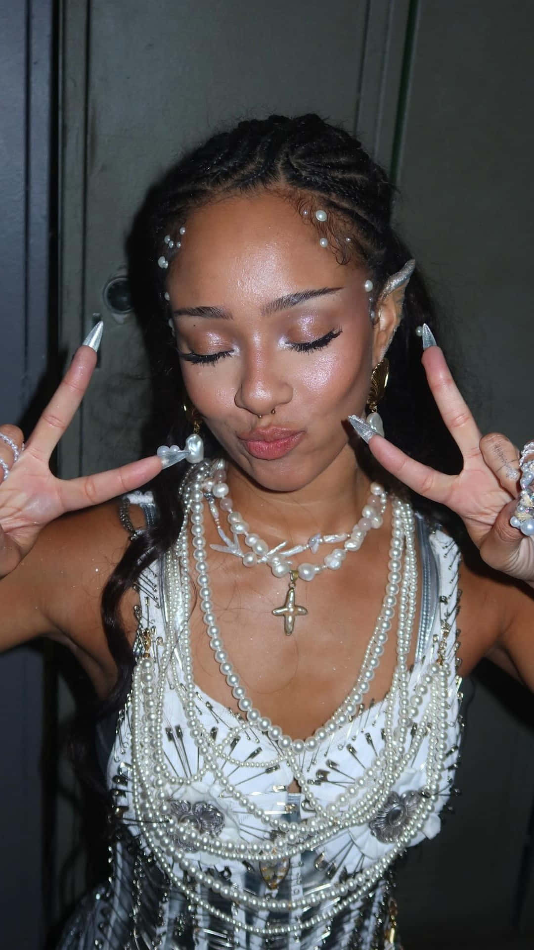  壁紙 — 一位辮子上飾有珍珠的女性，戴著多層珍珠首飾和長銀色指甲，做出和平手勢。