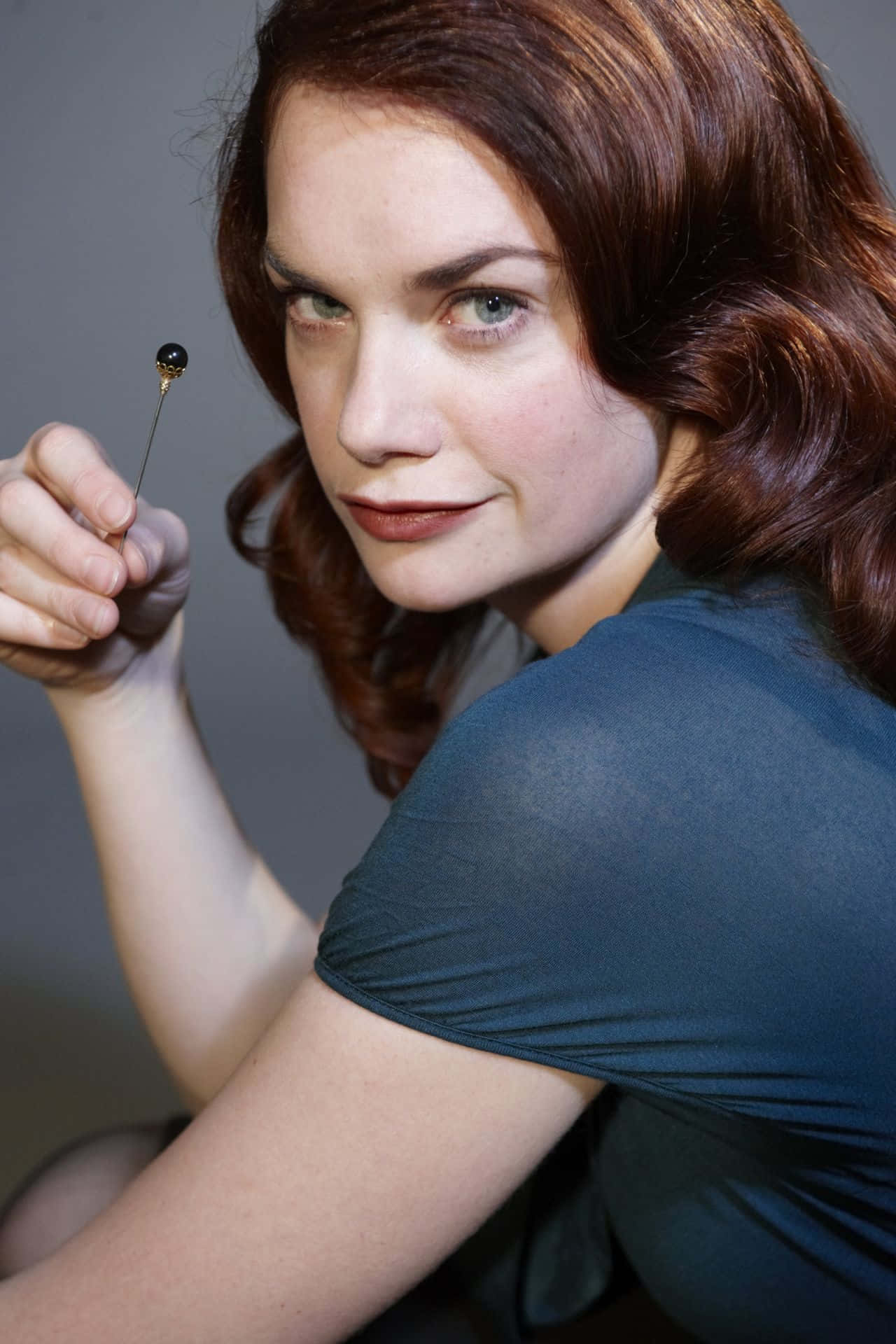 Ruth Wilson 桌布 壁紙 — 一位紅髮女性在工作室肖像中，對著灰色背景拿著一個小別針。