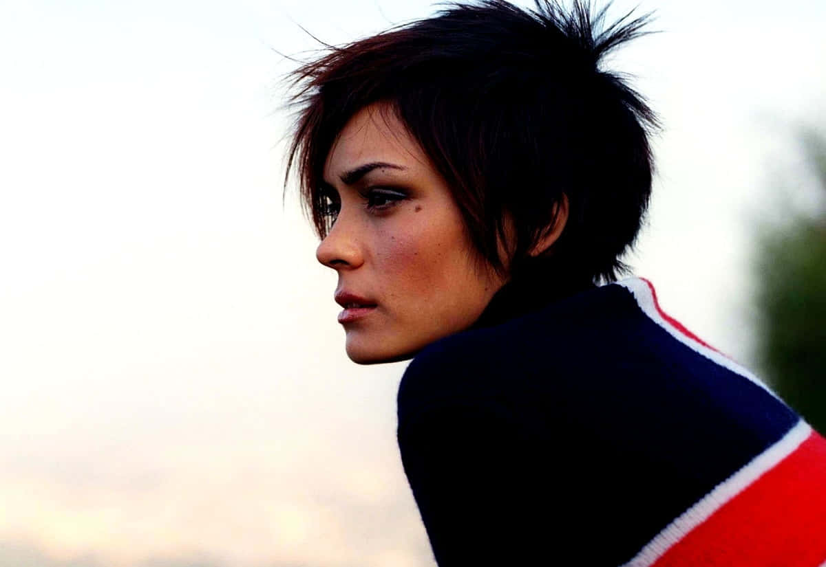 Shannyn Sossamon 桌布 壁紙 — 一位短黑髮、眼神強烈的女性，在柔和天空背景下看向鏡頭外。