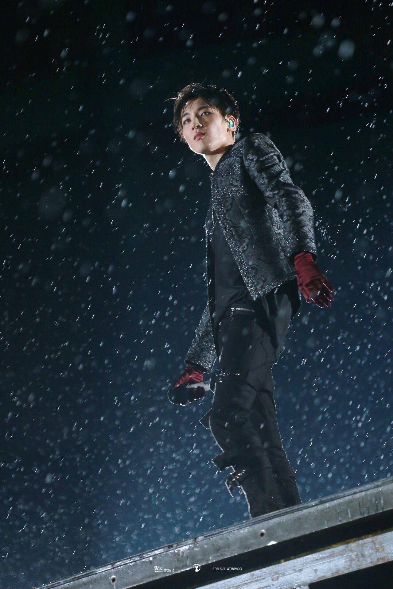 Wonwoo 雨中演出 壁紙 — 一位表演者夜晚站在舞台上，雪花飄落，身穿深色外套和紅色手套。