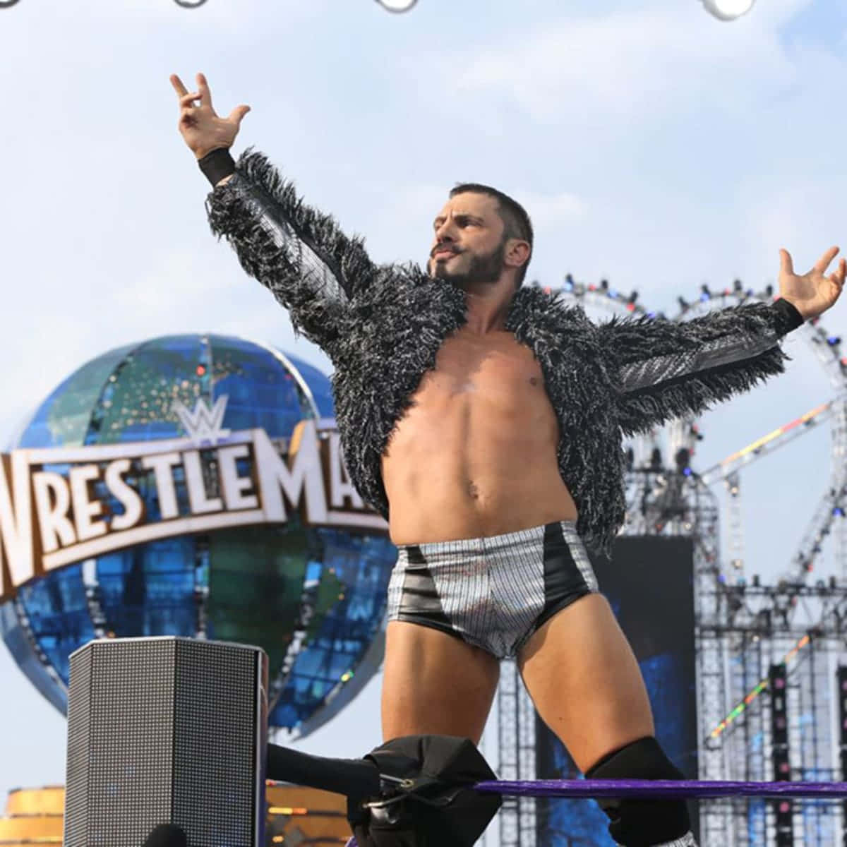 WrestleMania 奧斯汀·艾瑞斯 獲得 Cruiserweight 挑戰冠軍 壁紙 — 一位肌肉發達的摔角手穿著羽毛外套和閃亮短褲，在WrestleMania的擂台角柱頂端擺出勝利姿勢。